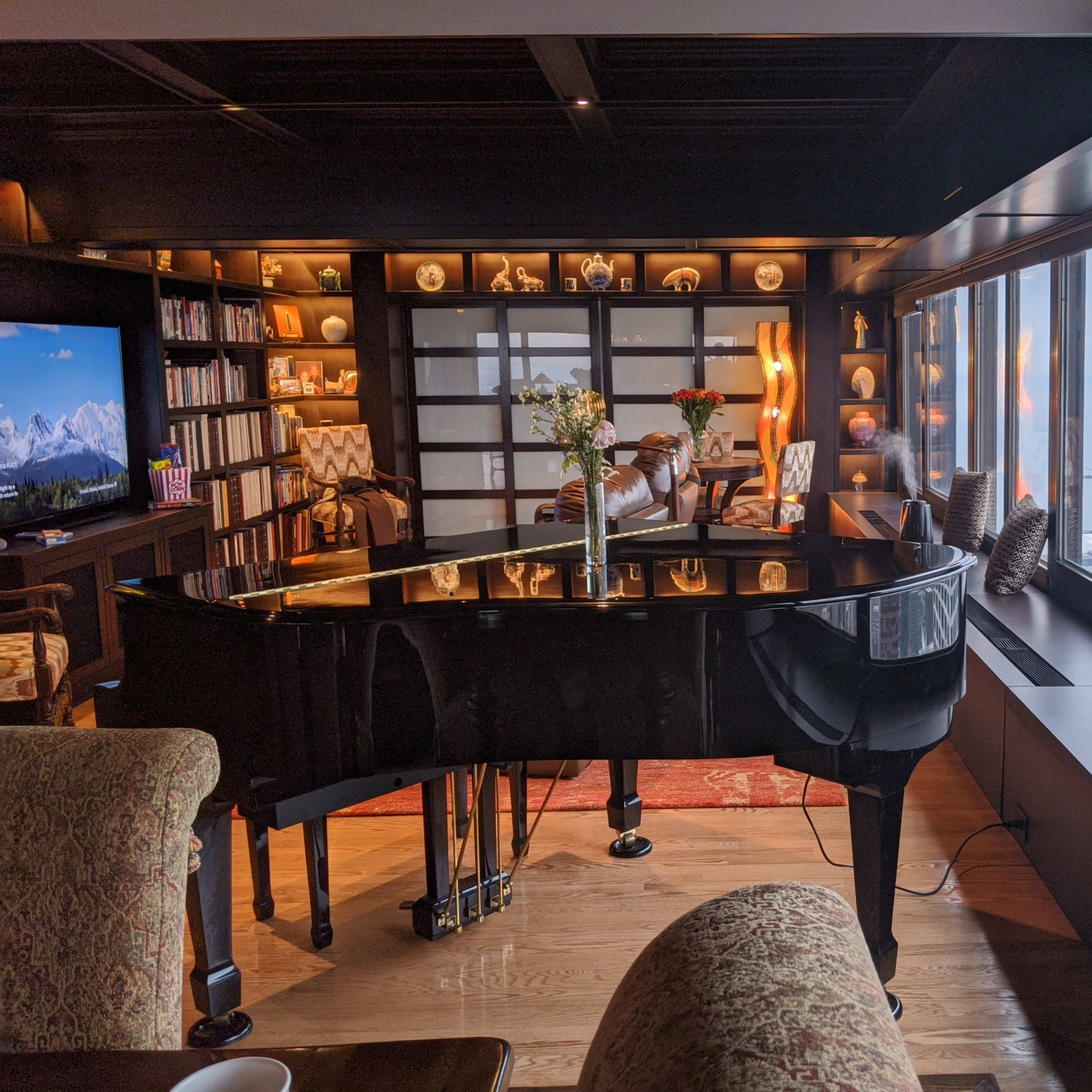 A grand piano sits in a stylishly decorated living room with large windows overlooking a seaside view.