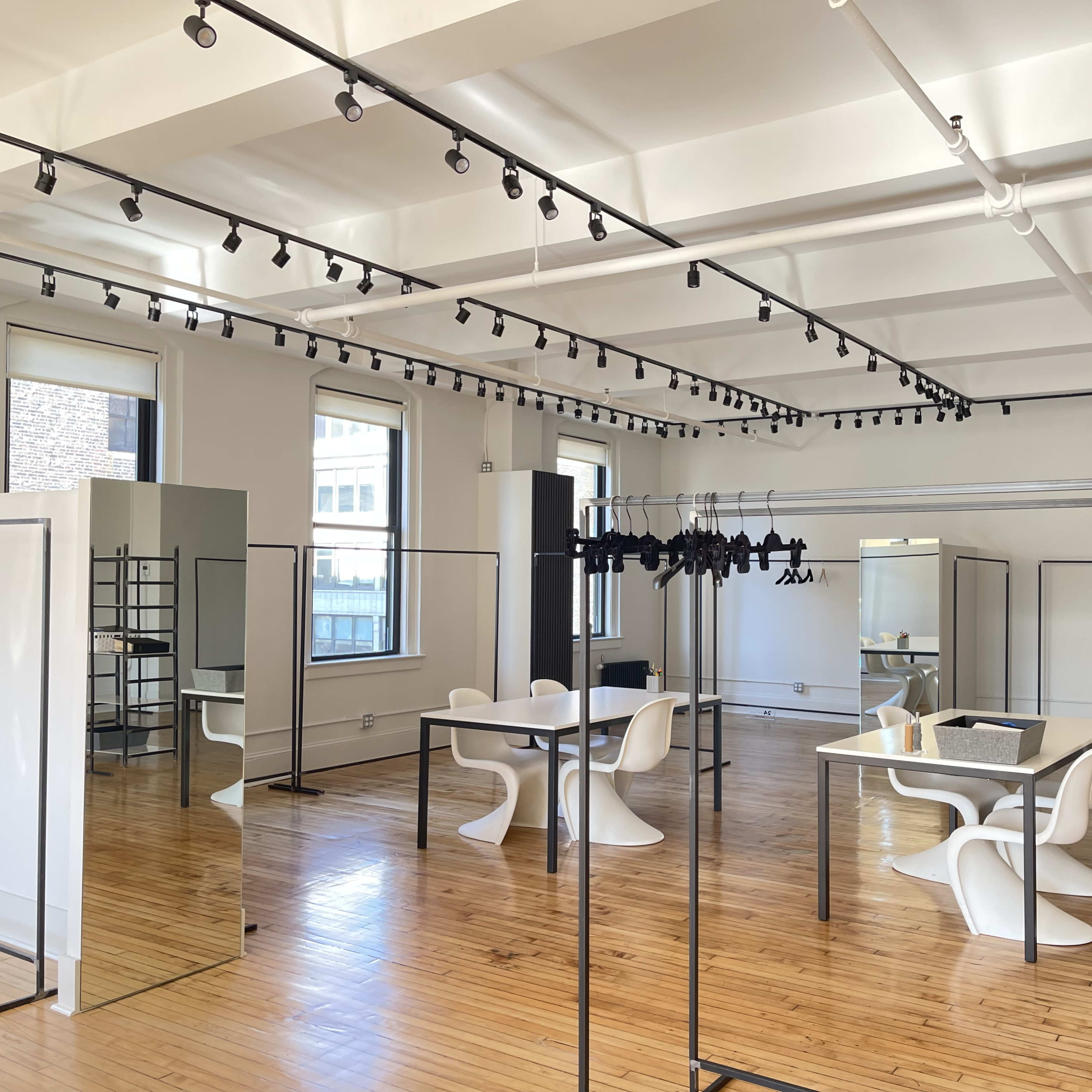 A well-lit, modern interior space with wooden floors, featuring minimalist furniture and multiple clothing racks.