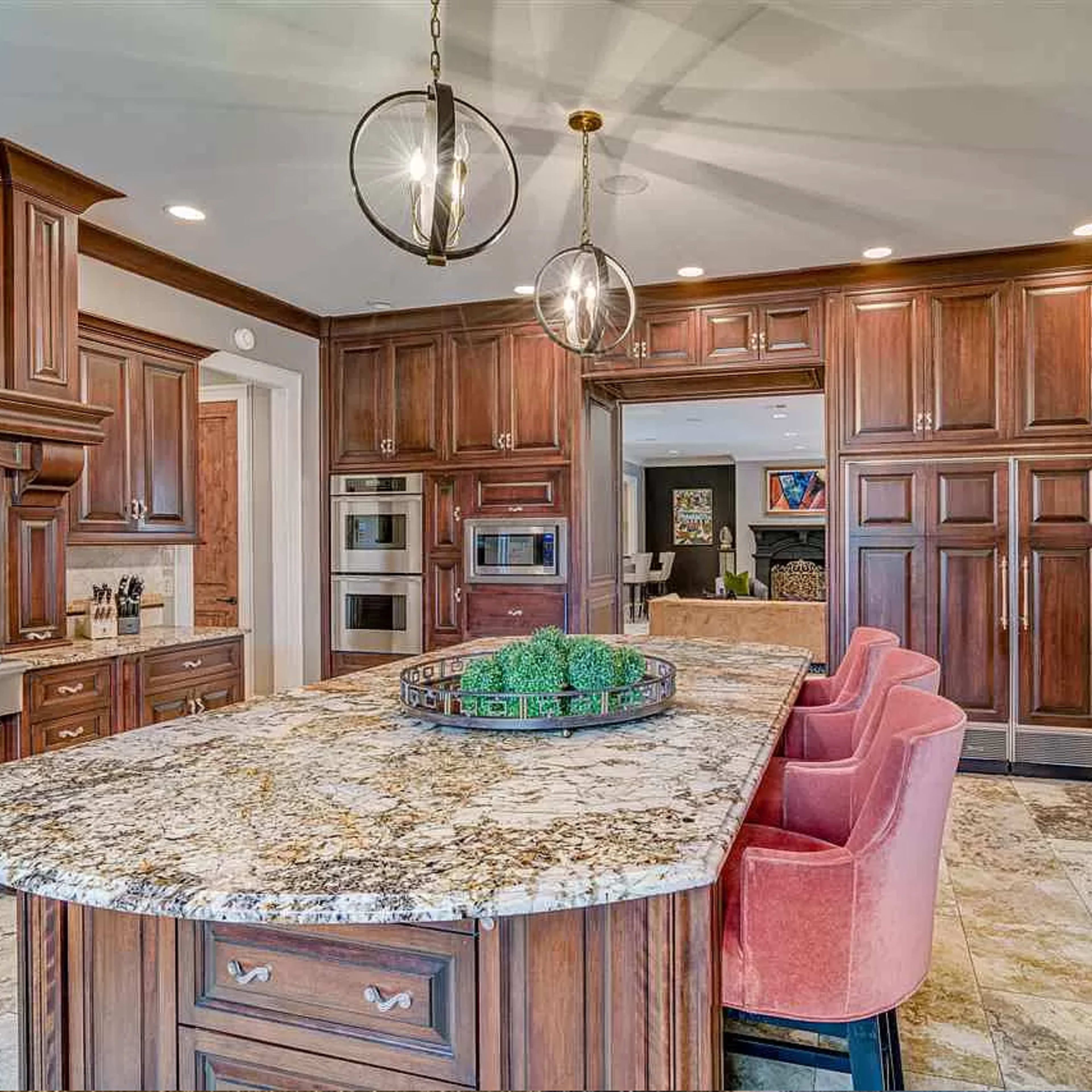 A spacious kitchen featuring dark wooden cabinets, a large granite island with pink seating, and modern appliances.
