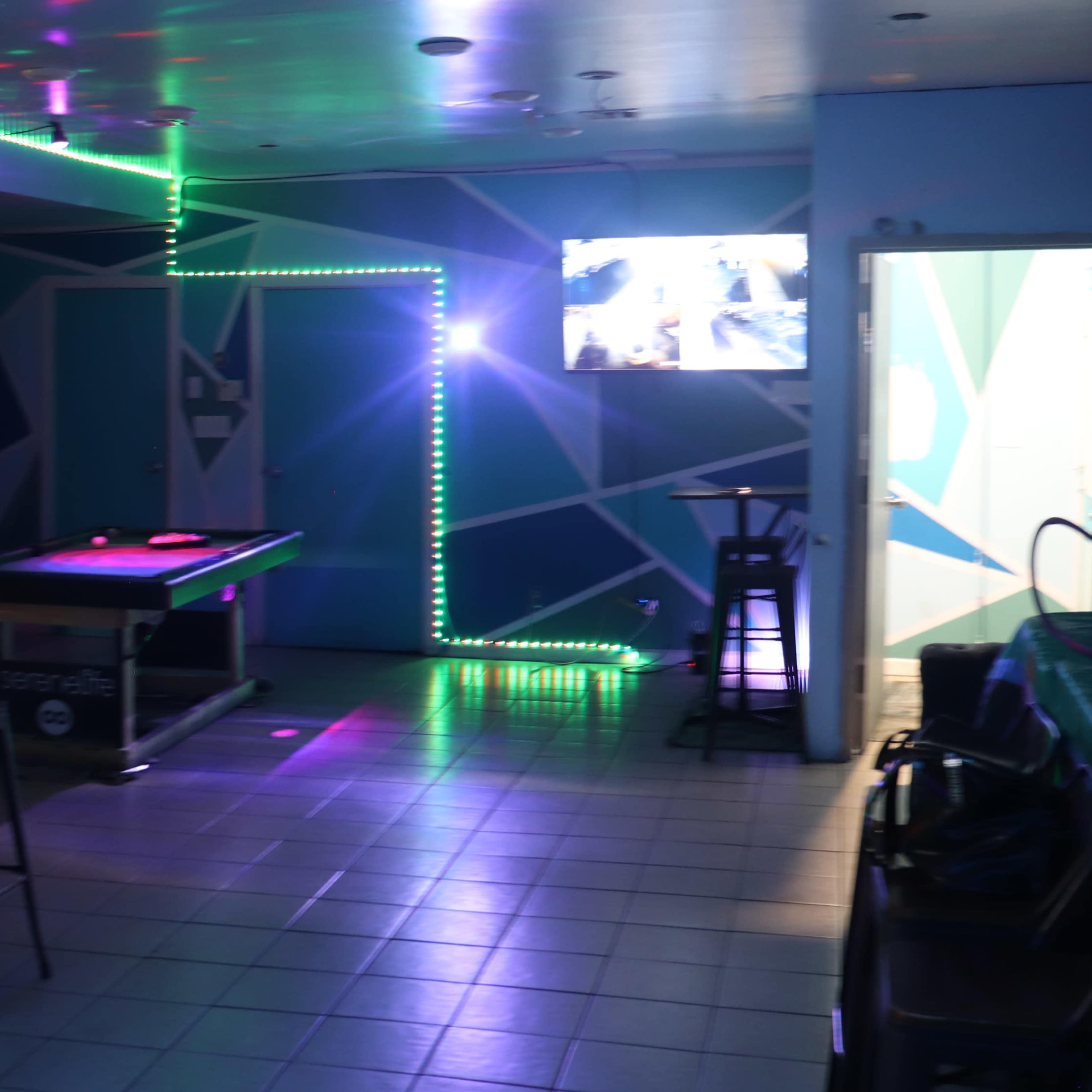 A room with colorful LED lights, a pool table, and a television mounted on the wall.
