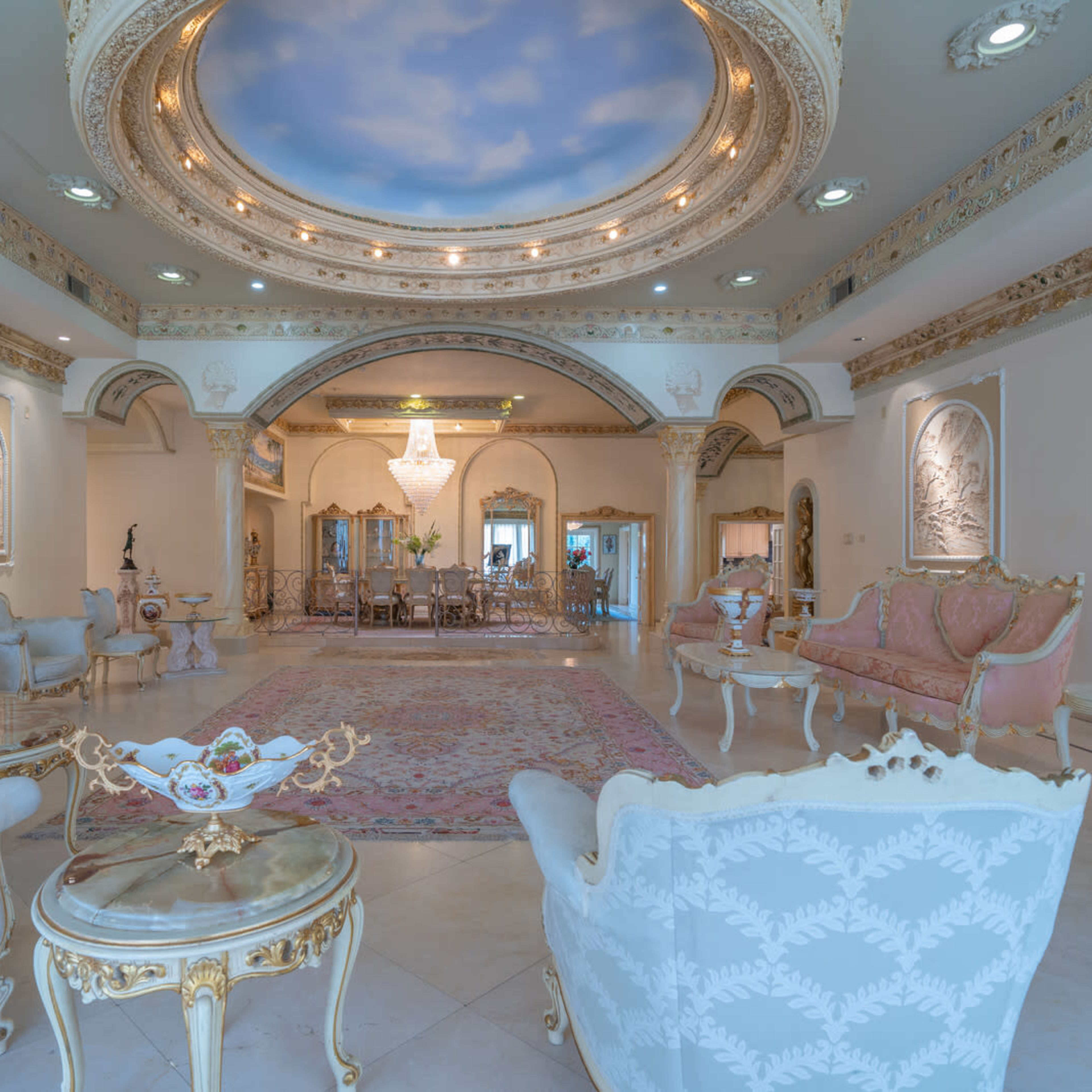 The scene depicts an ornate living room with elegant furniture, intricate moldings, and a large chandelier, complemented by a view of a sky mural on the ceiling.