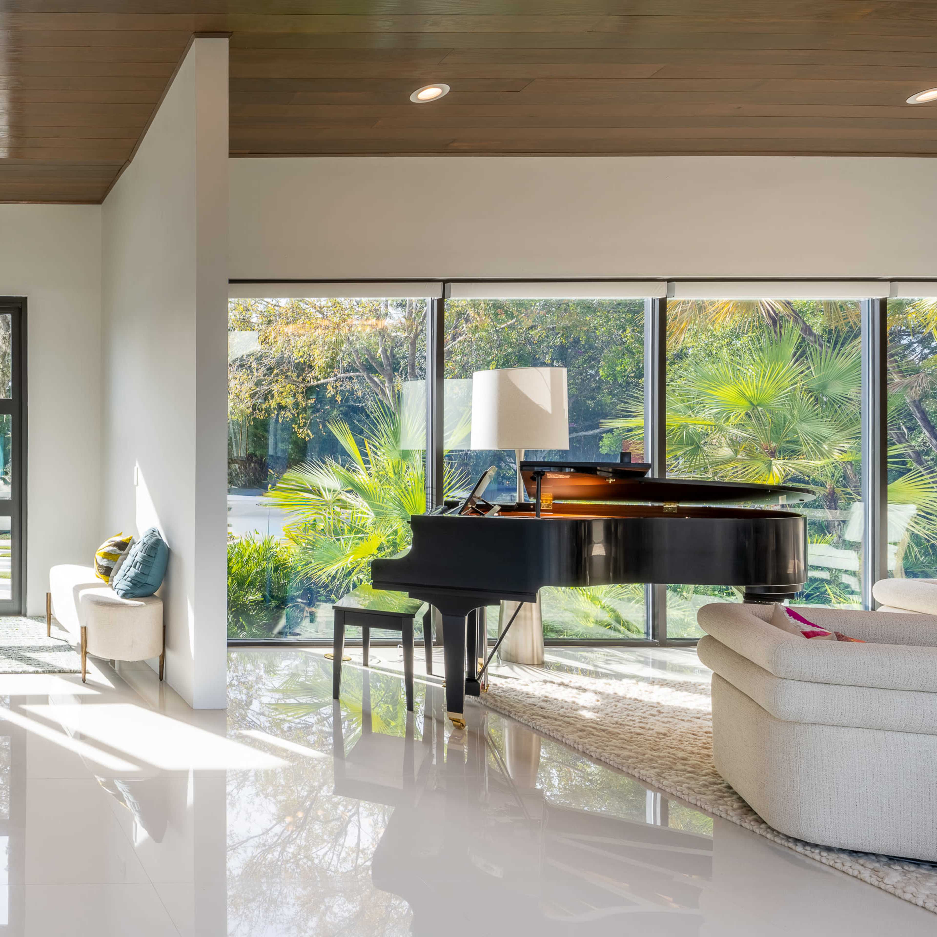 A bright, modern living room with large windows, a grand piano, and minimalistic furniture.