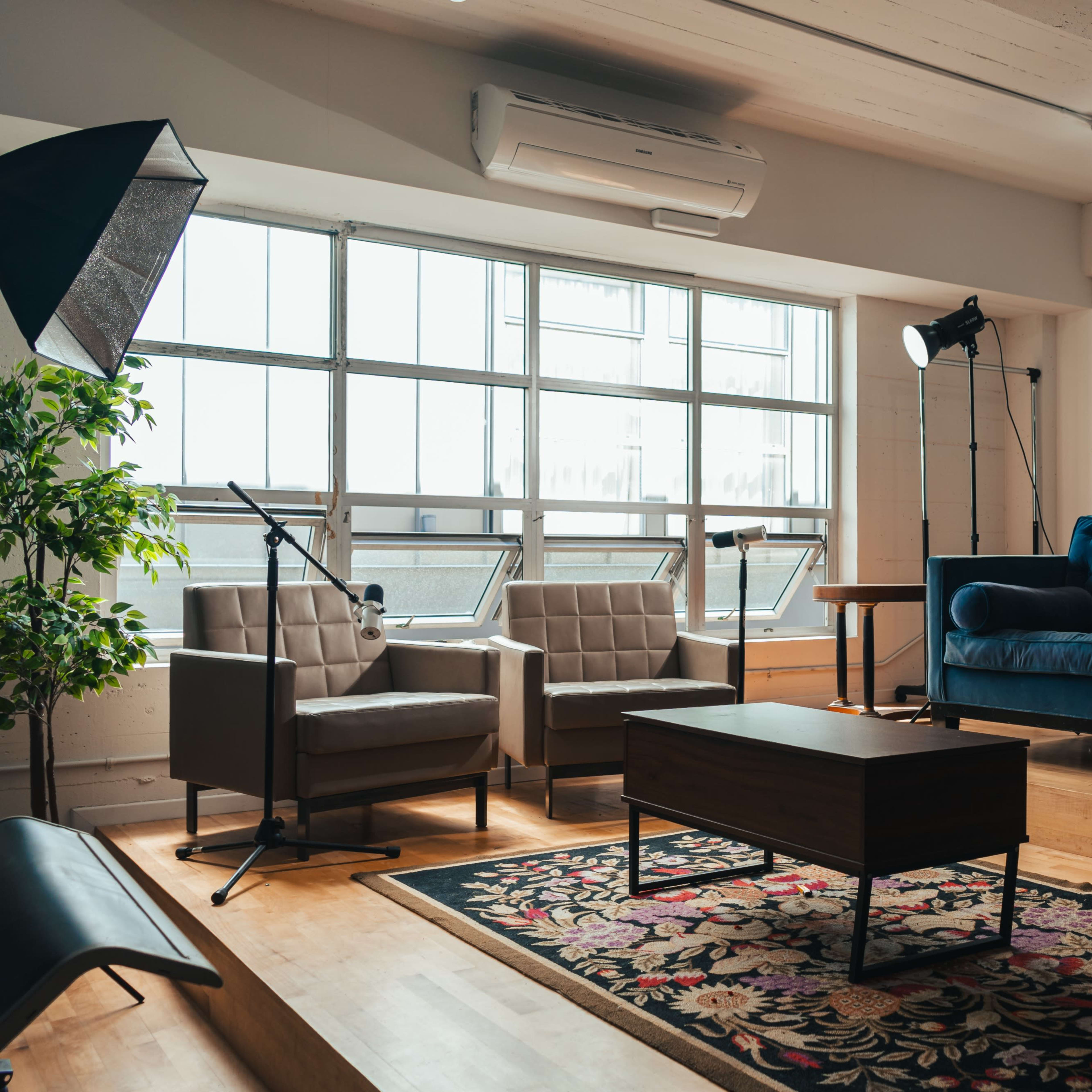 A modern living room with a blue sofa, two armchairs, a coffee table, and large windows allowing natural light.
