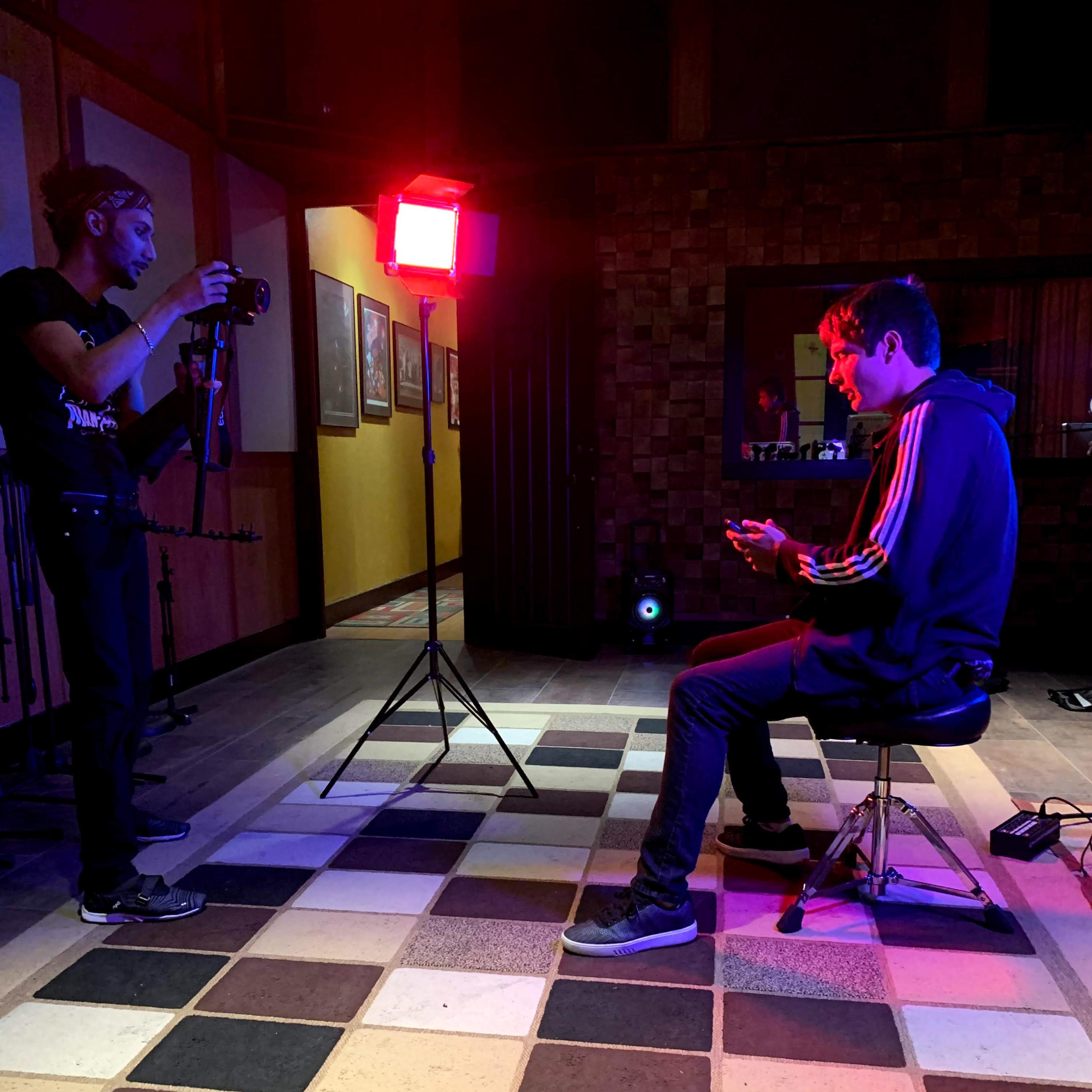 A photographer captures an individual seated on a stool, illuminated by a red light in a dimly lit room.
