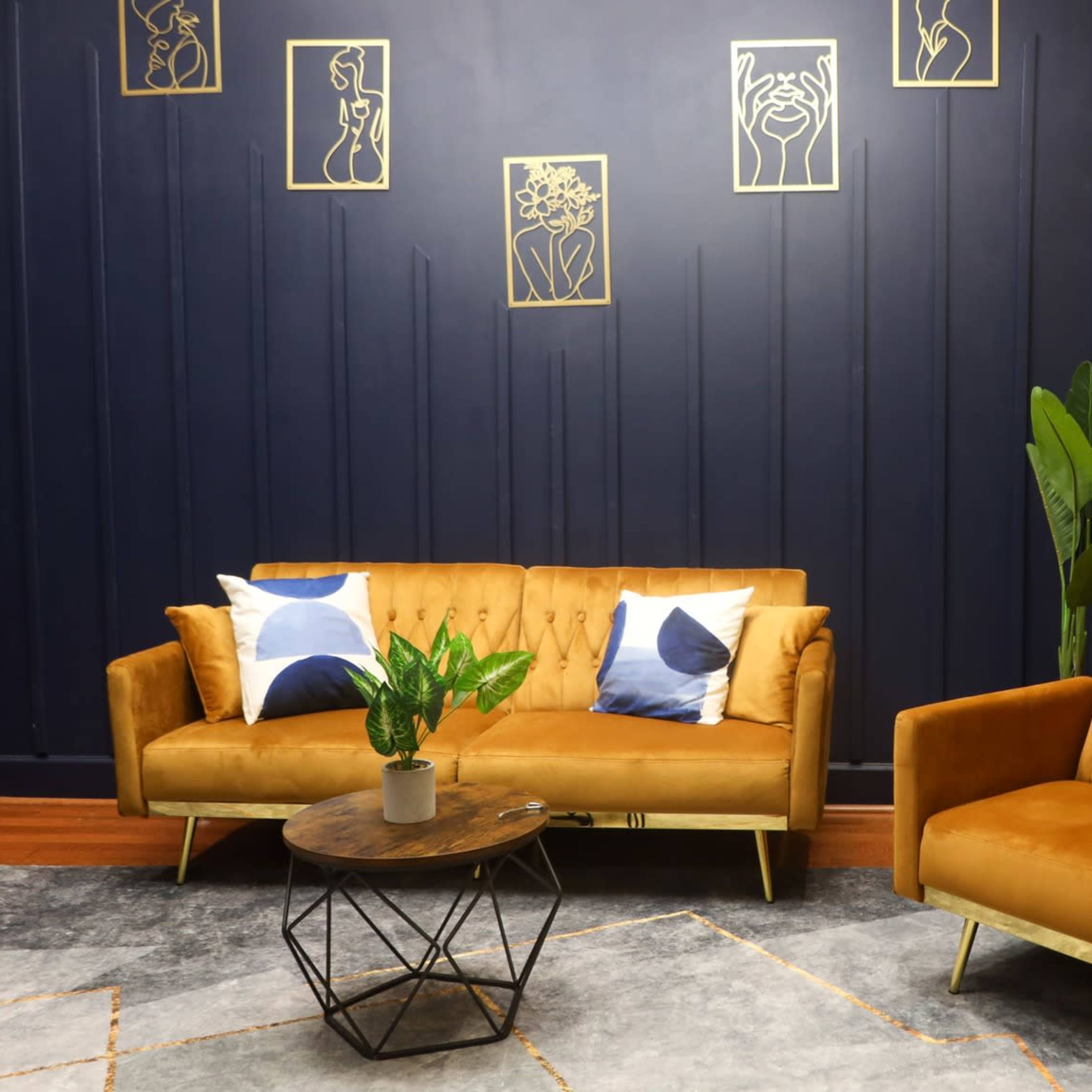 A modern sitting area with a mustard-yellow wall, navy-blue accents, a brown velvet sofa and armchair, a round coffee table, and decorative wall art.