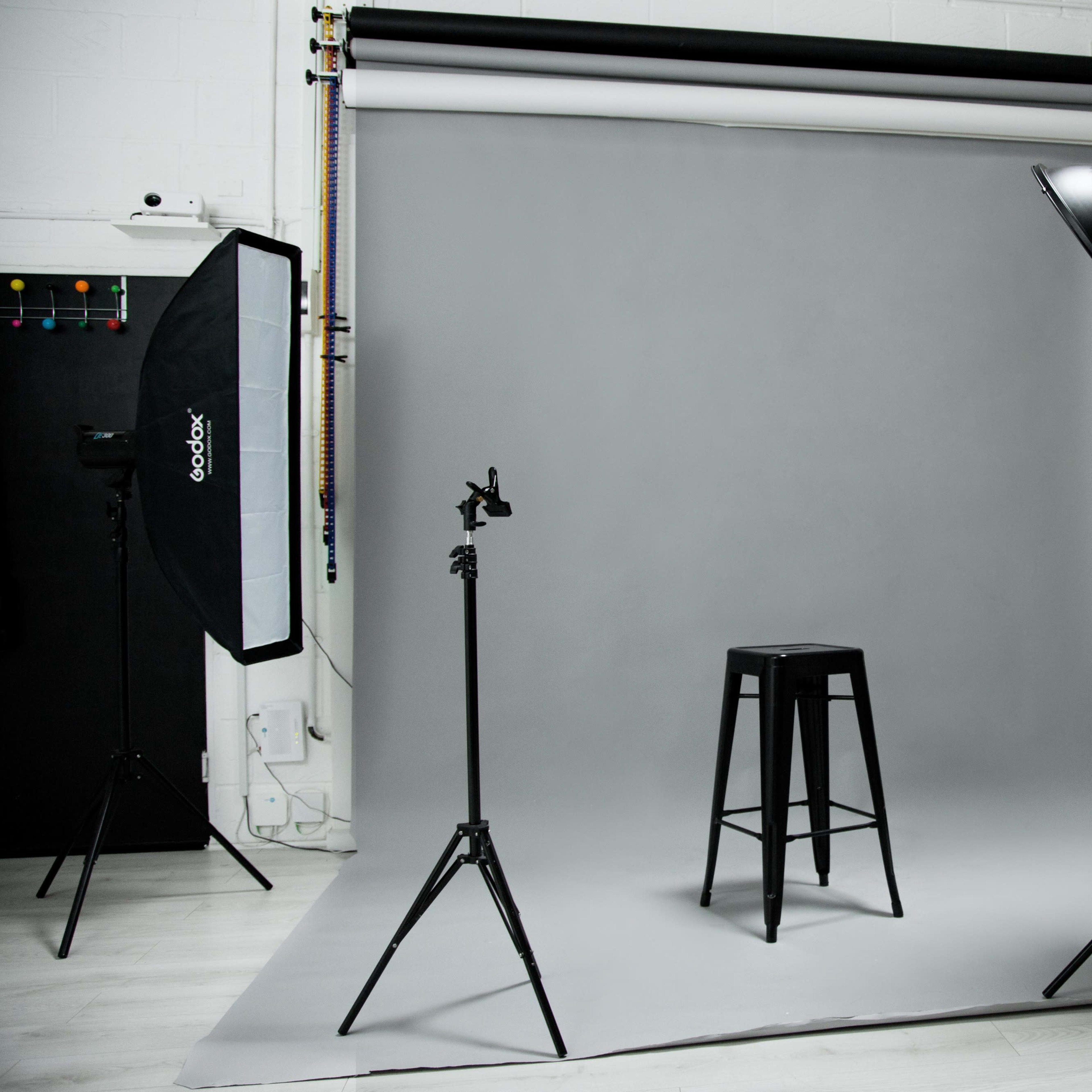 A photography studio setup featuring a gray backdrop, a black stool, and multiple lighting equipment.