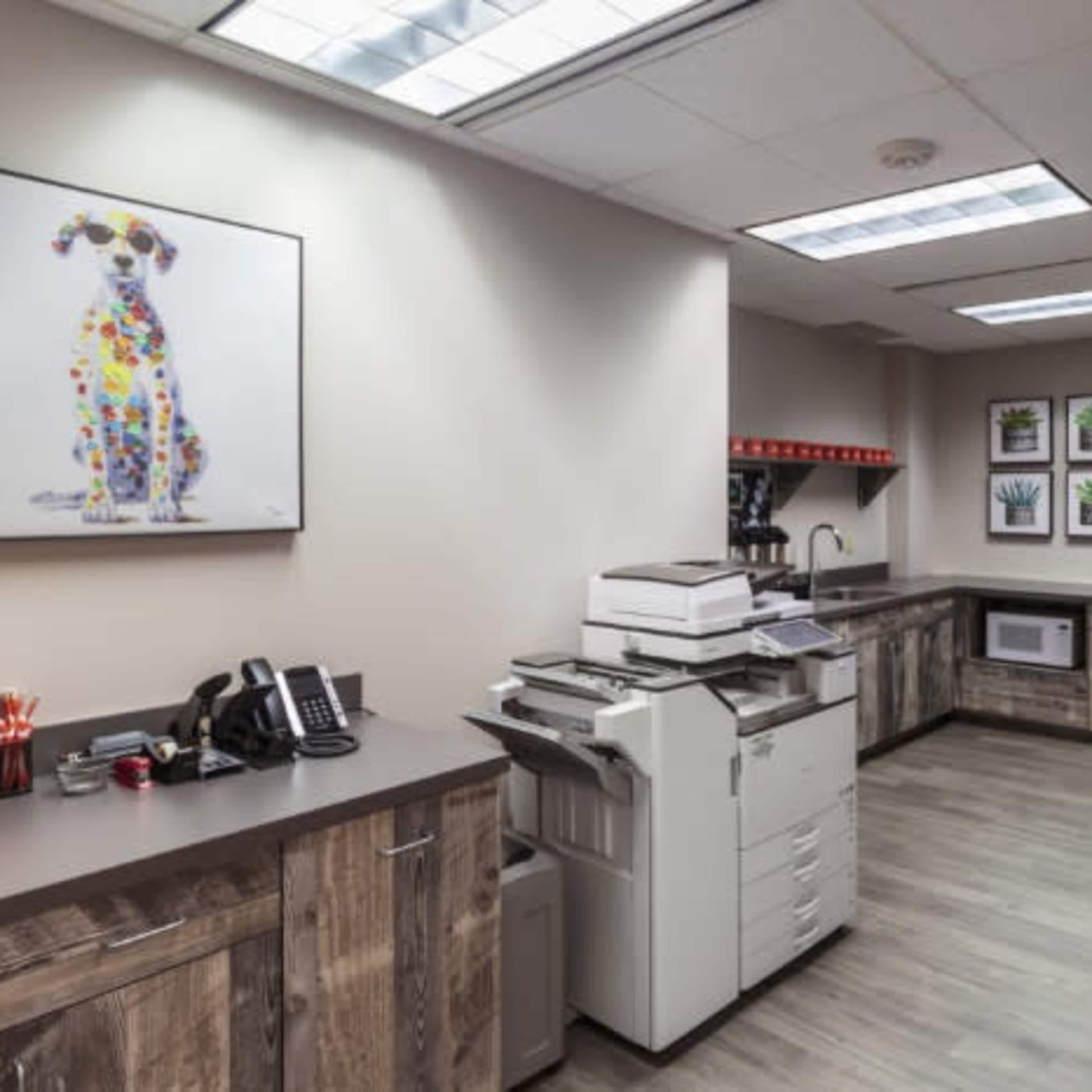 An office break room featuring a copier, a refrigerator, a microwave, and framed artwork on the walls.
