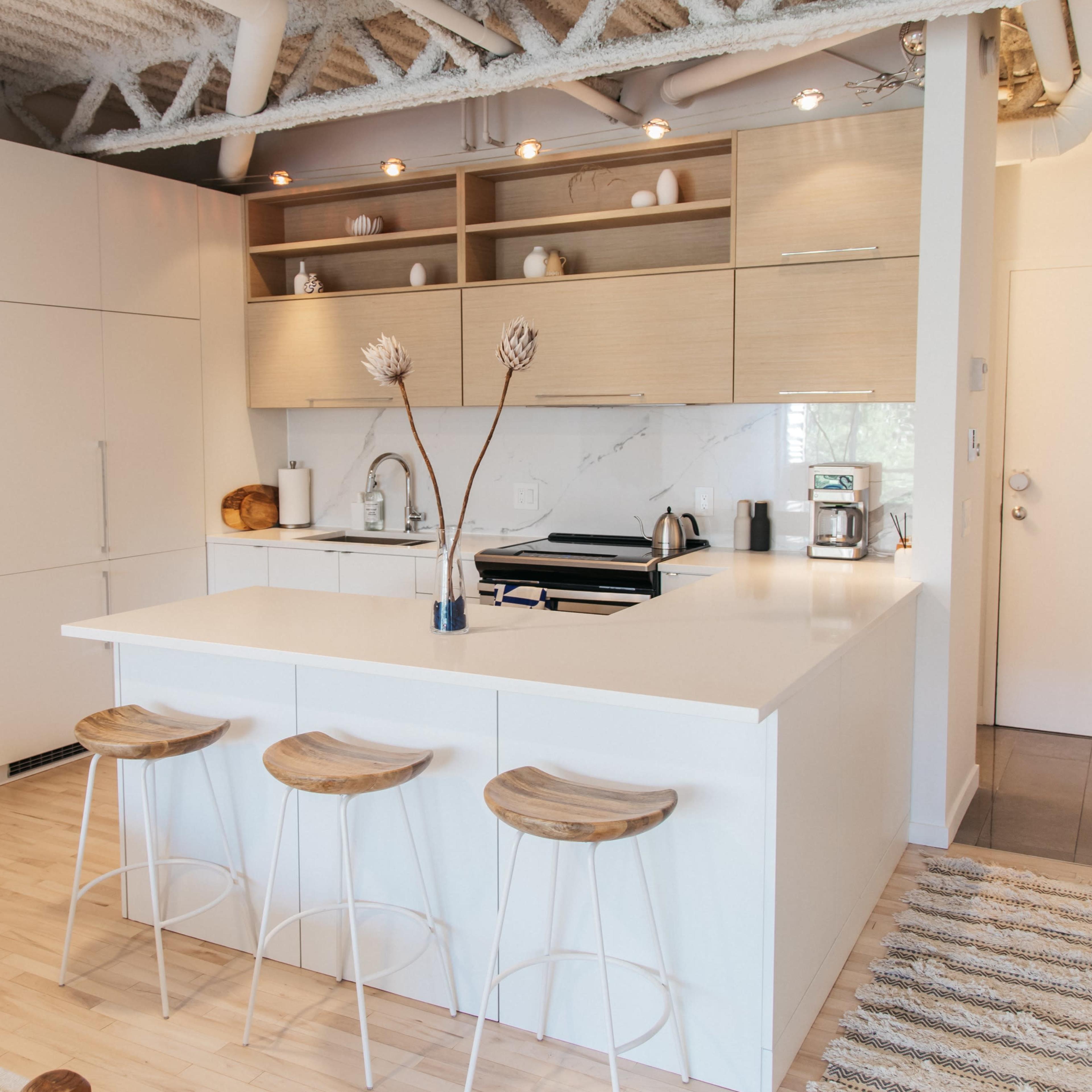 A modern kitchen featuring a white island with three wooden stools, beige cabinetry, and a sleek countertop with minimal decor.