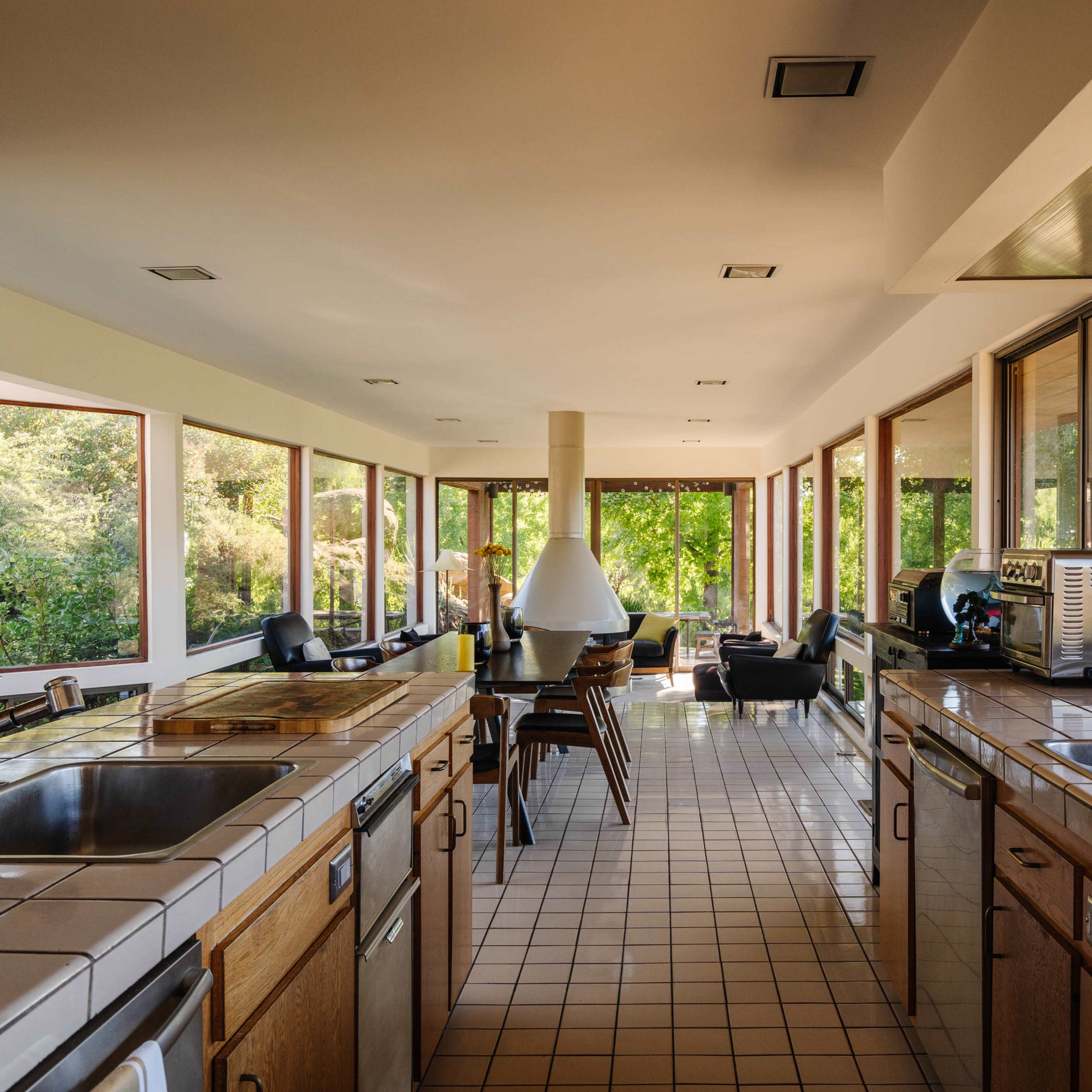 A spacious kitchen with two sink islands, large windows overlooking greenery, and an arrangement of modern dining furniture.