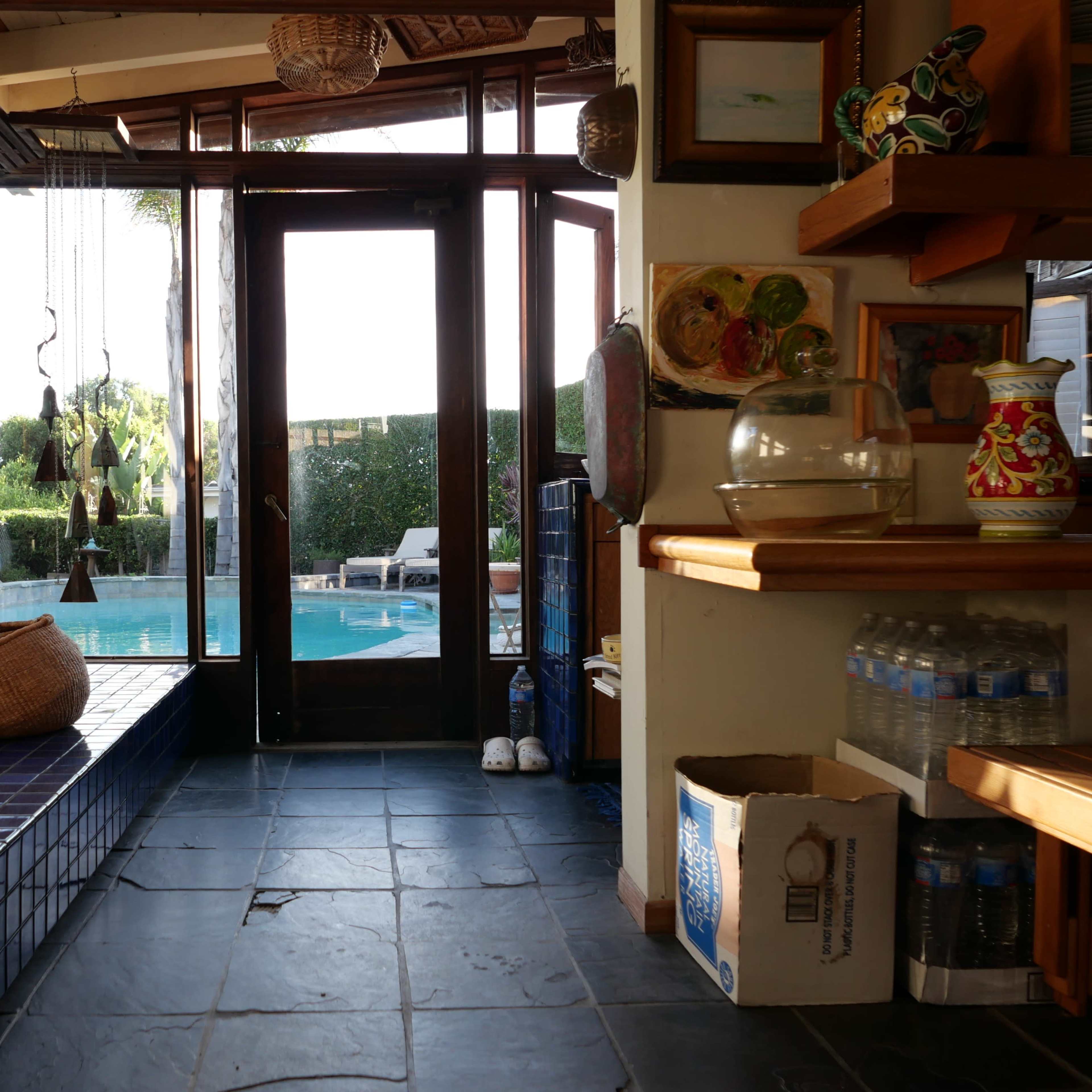 A view from inside a house towards a swimming pool area, with a combination of tiled surfaces and wooden accents.