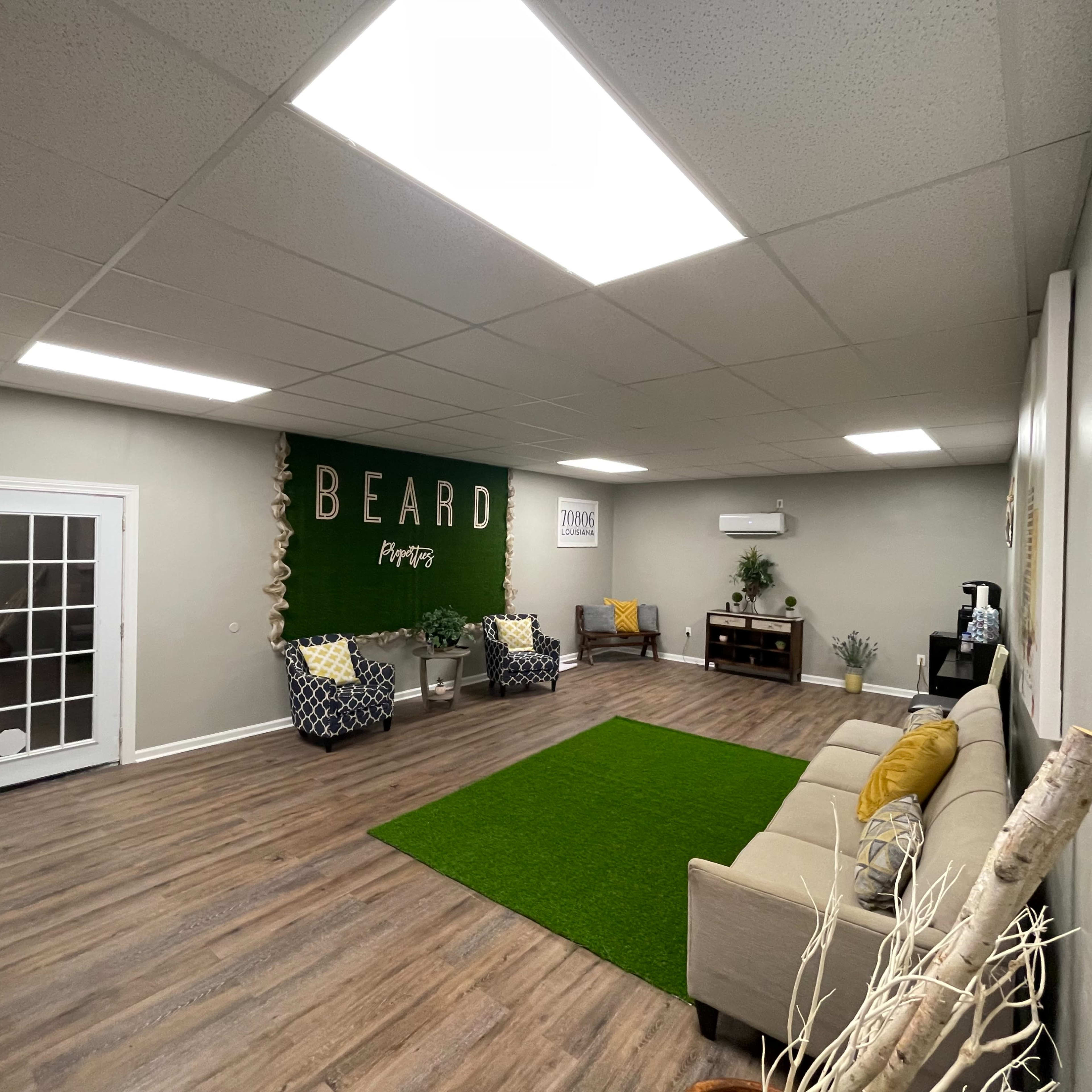The room features a green carpet area, light-colored couches, and a wall with the word "BEARD" prominently displayed, along with two seating areas.
