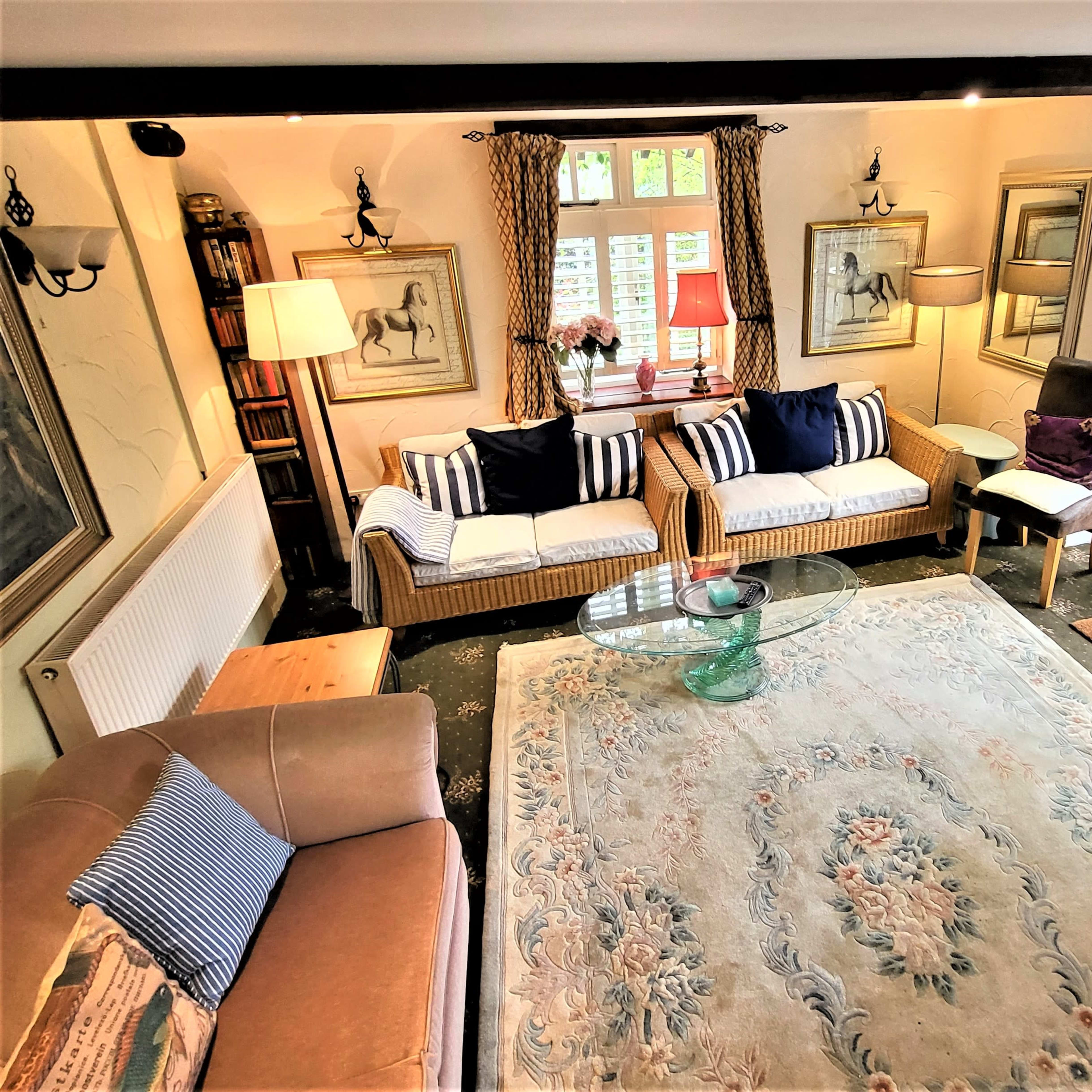 A cozy living room with two rattan sofas, various lamps, and a glass coffee table centered on a large area rug.