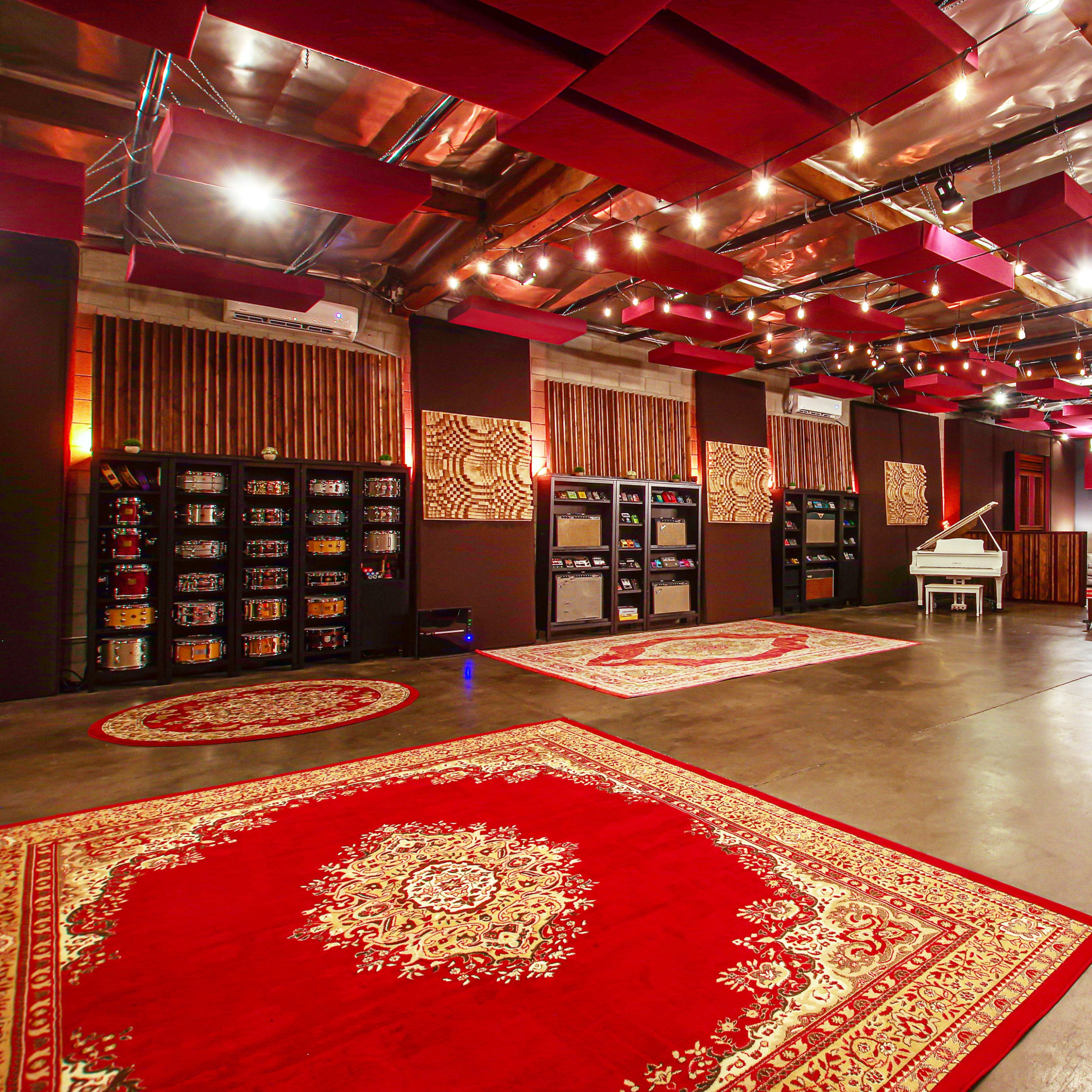 A spacious interior room designed for music or sound production, featuring red patterned rugs, dark walls, and acoustic panels on the ceiling.