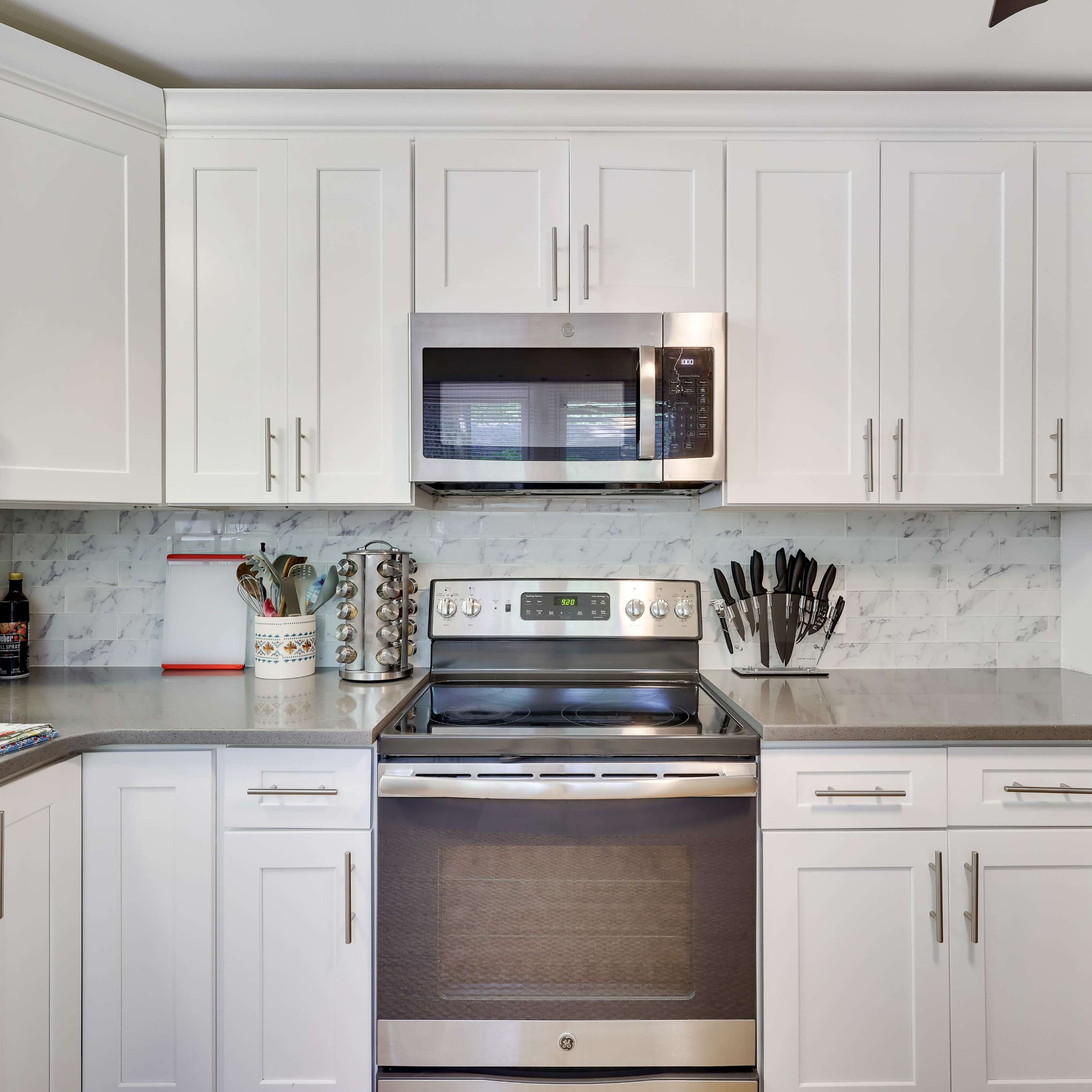 A modern kitchen with white cabinets, stainless steel appliances, and a marble backsplash.
