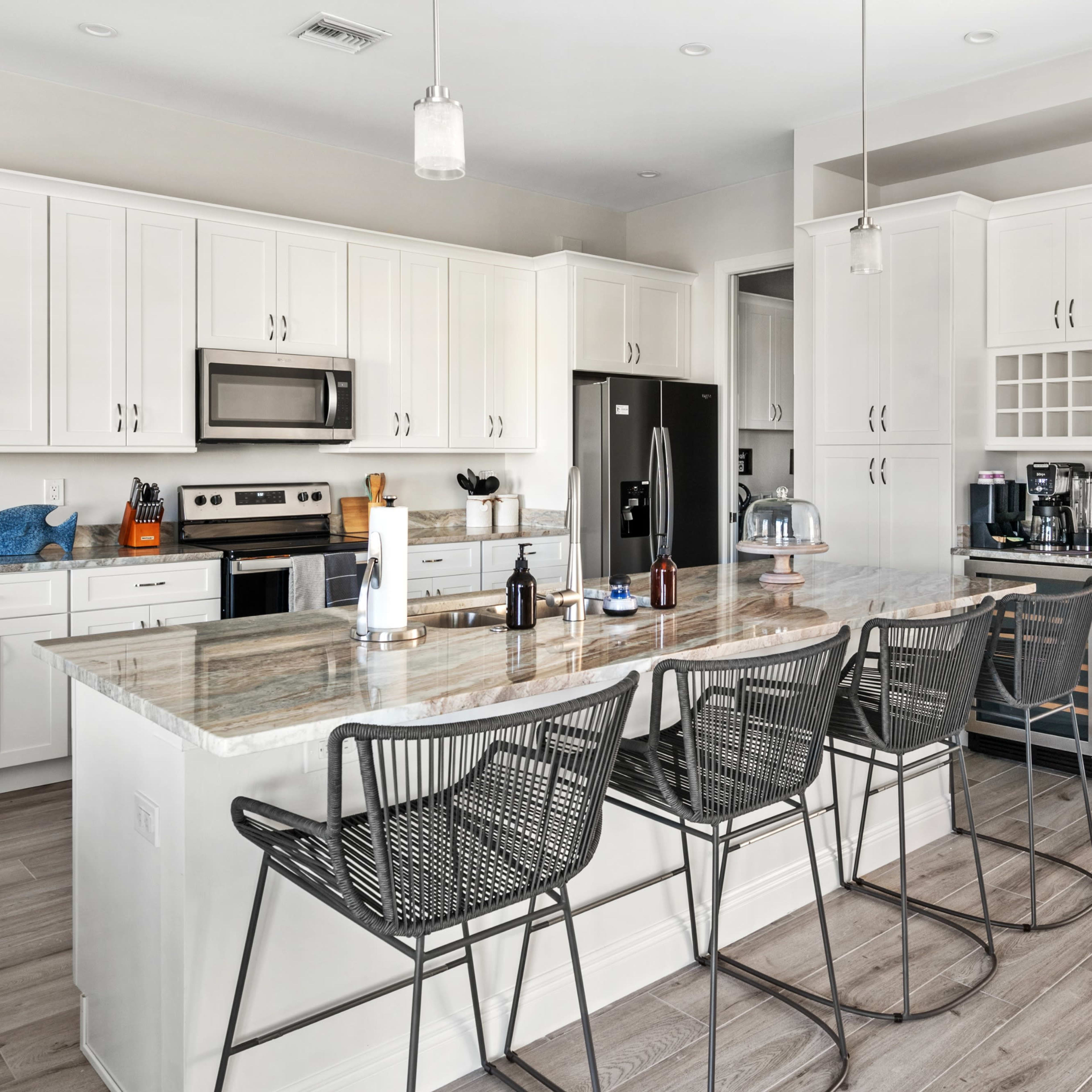 A modern kitchen features white cabinetry, stainless steel appliances, a large island with bar seating, and a light-colored wooden floor.