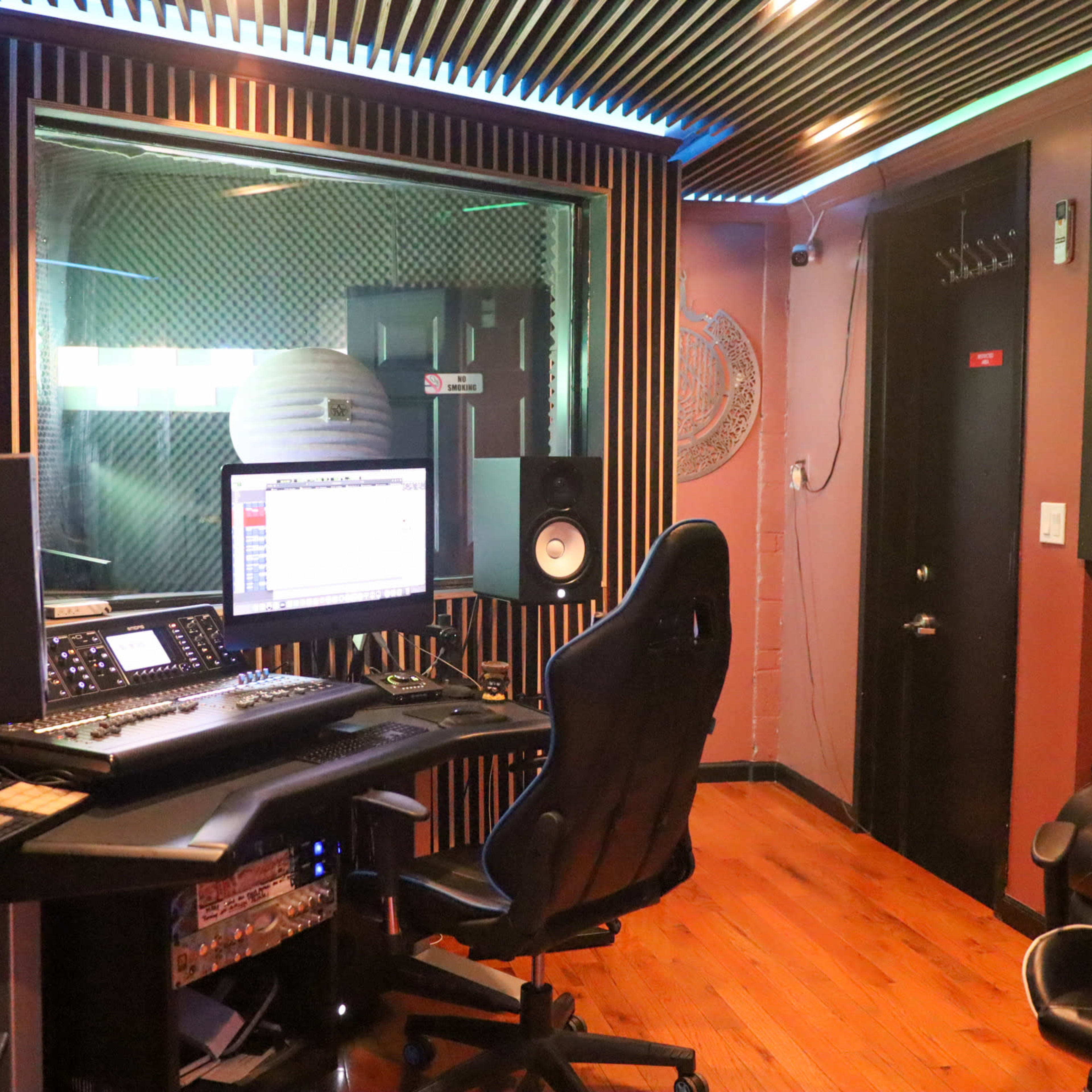 A recording studio with a computer setup, sound equipment, and a black office chair in a room with soundproof walls.