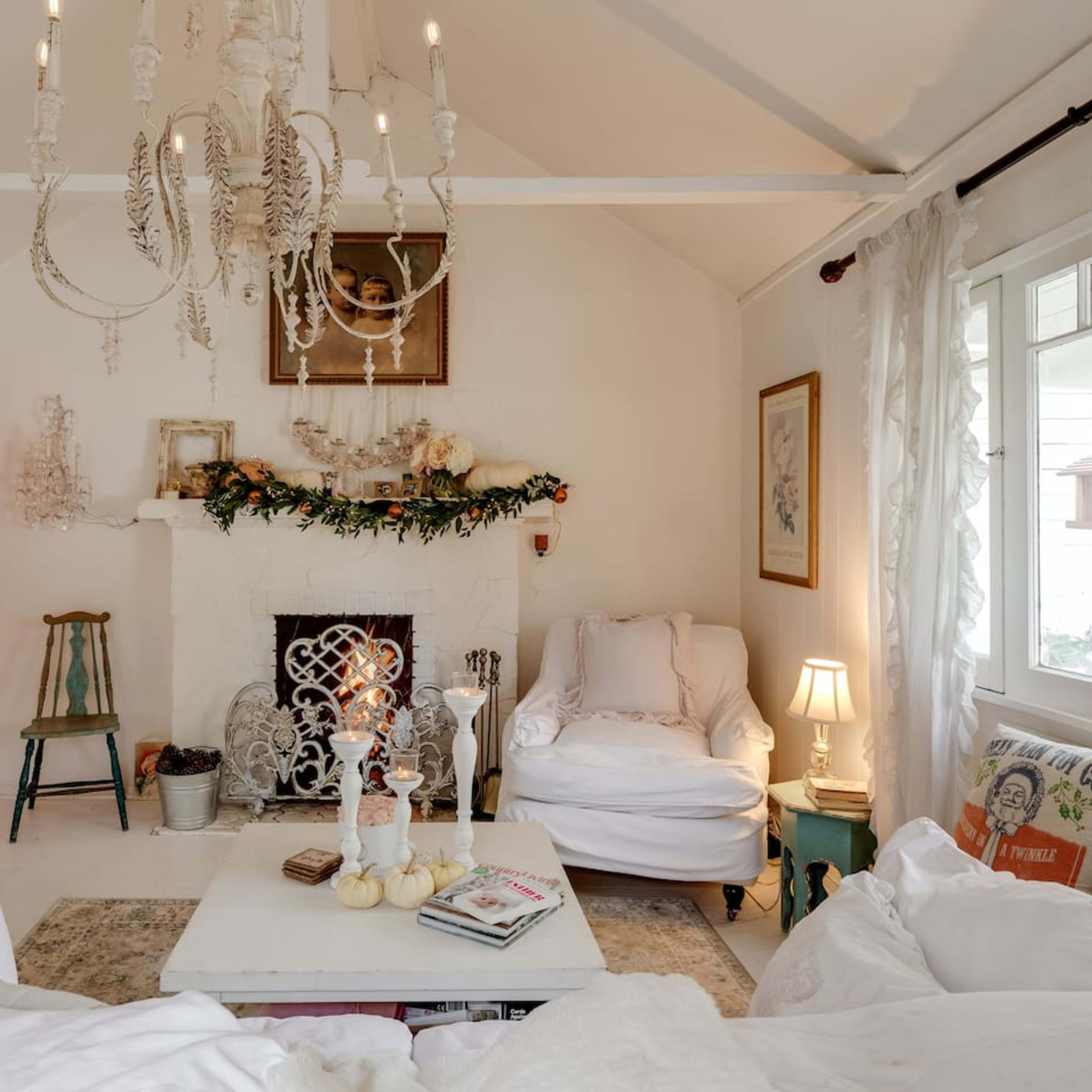 A cozy living room features white furniture, a chandelier, and a decorated fireplace with seasonal greenery.