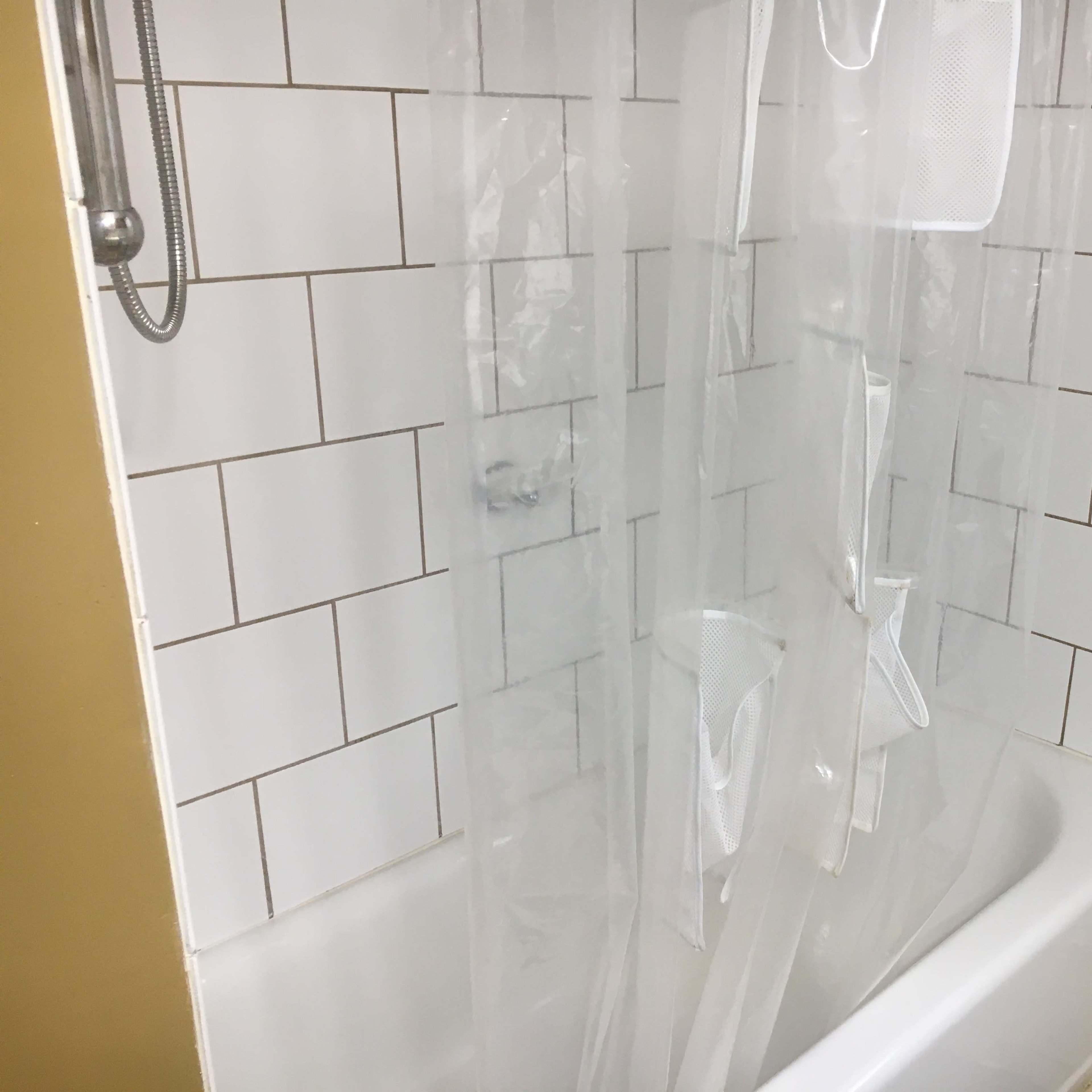 A bathtub surrounded by white tiled walls and a transparent shower curtain hanging in front.