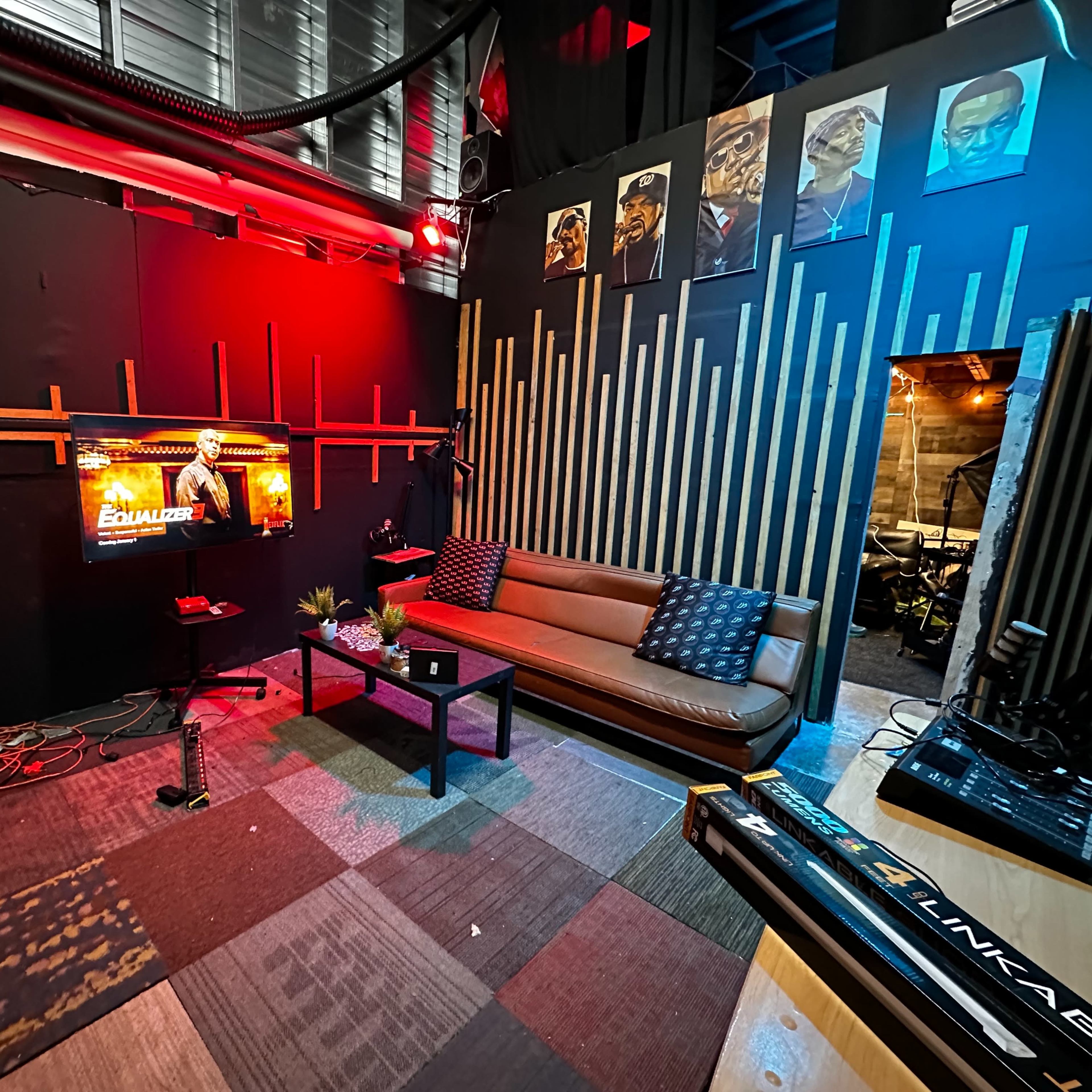 A small studio room with a brown couch, a coffee table, a television displaying a character, and a decorated wall featuring framed portraits.