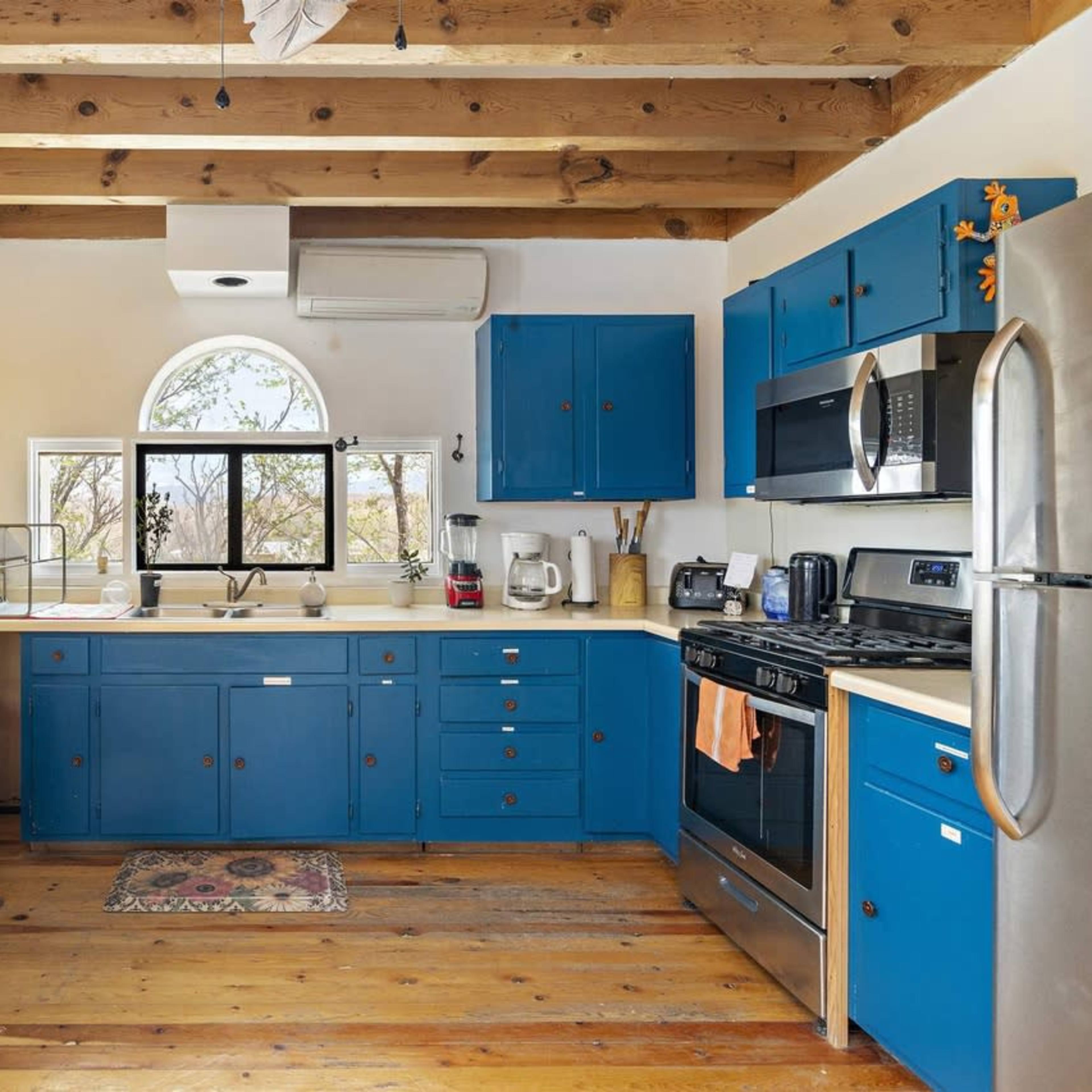 The kitchen features blue cabinetry, stainless steel appliances, and wooden beams on the ceiling.
