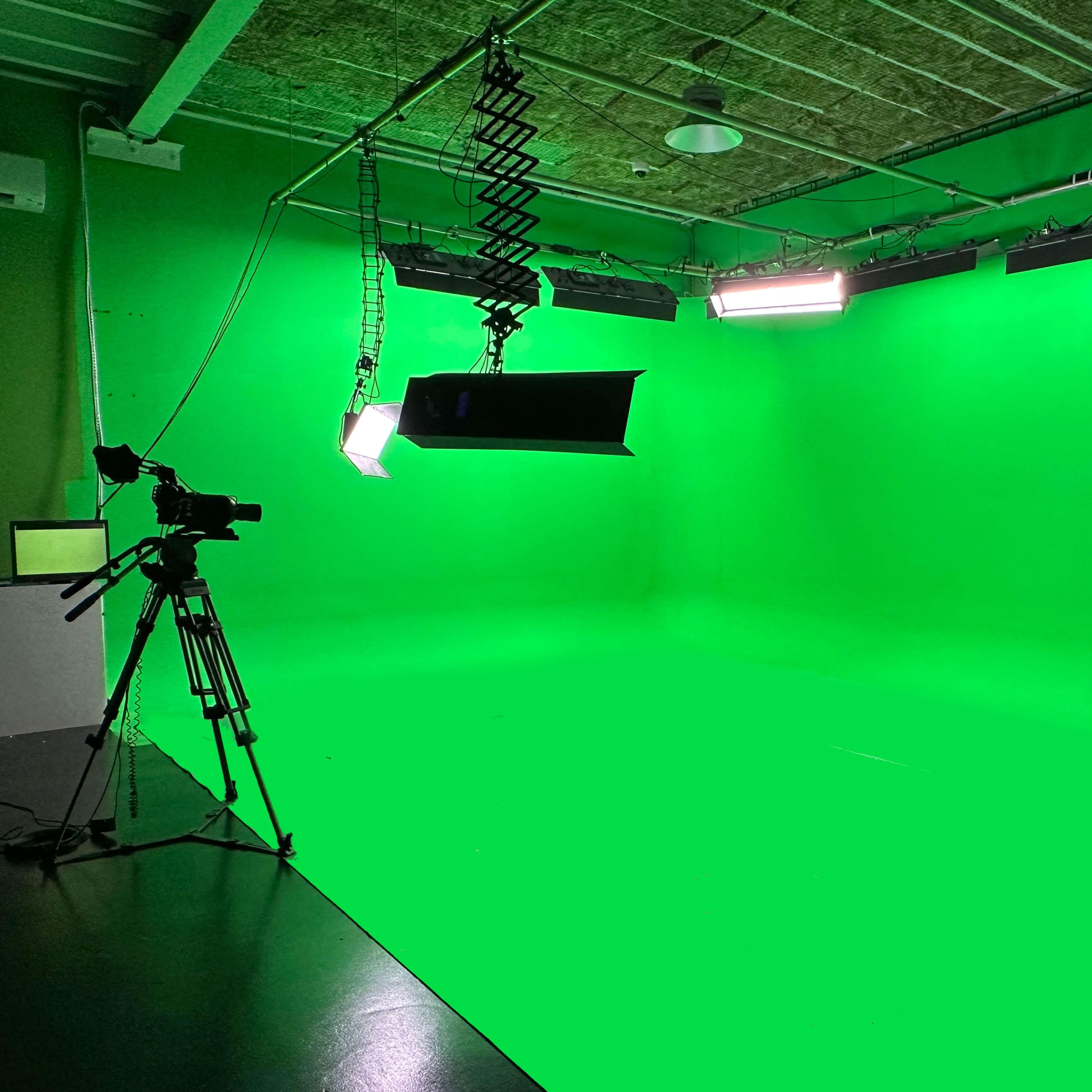 A green screen studio with a camera and lighting equipment set up.