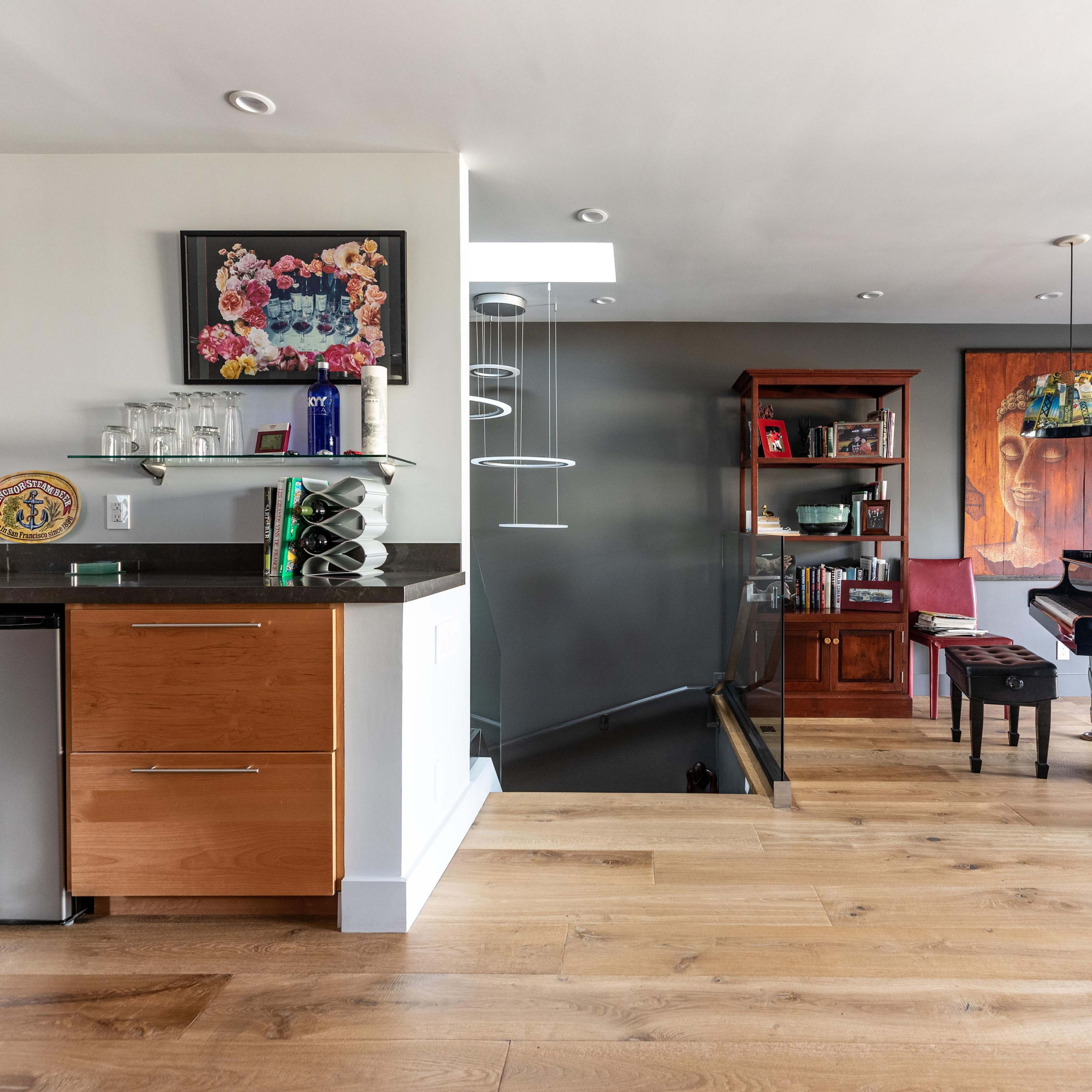 A modern interior featuring a kitchen area with a bar and a grand piano in a living space with wooden flooring and artistic decor.