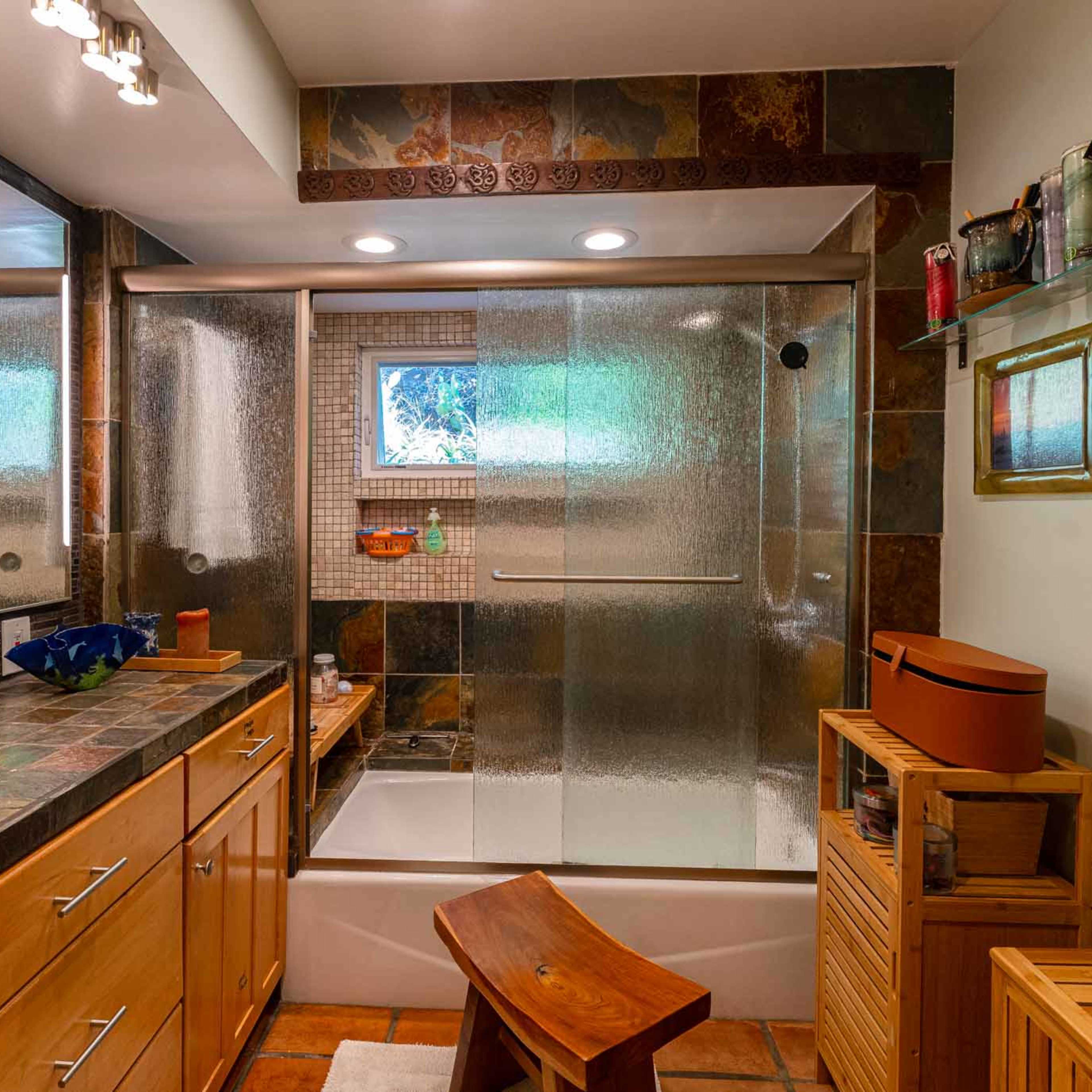 A well-lit bathroom features a shower area with glass doors, a bathtub, and a wooden vanity with storage.