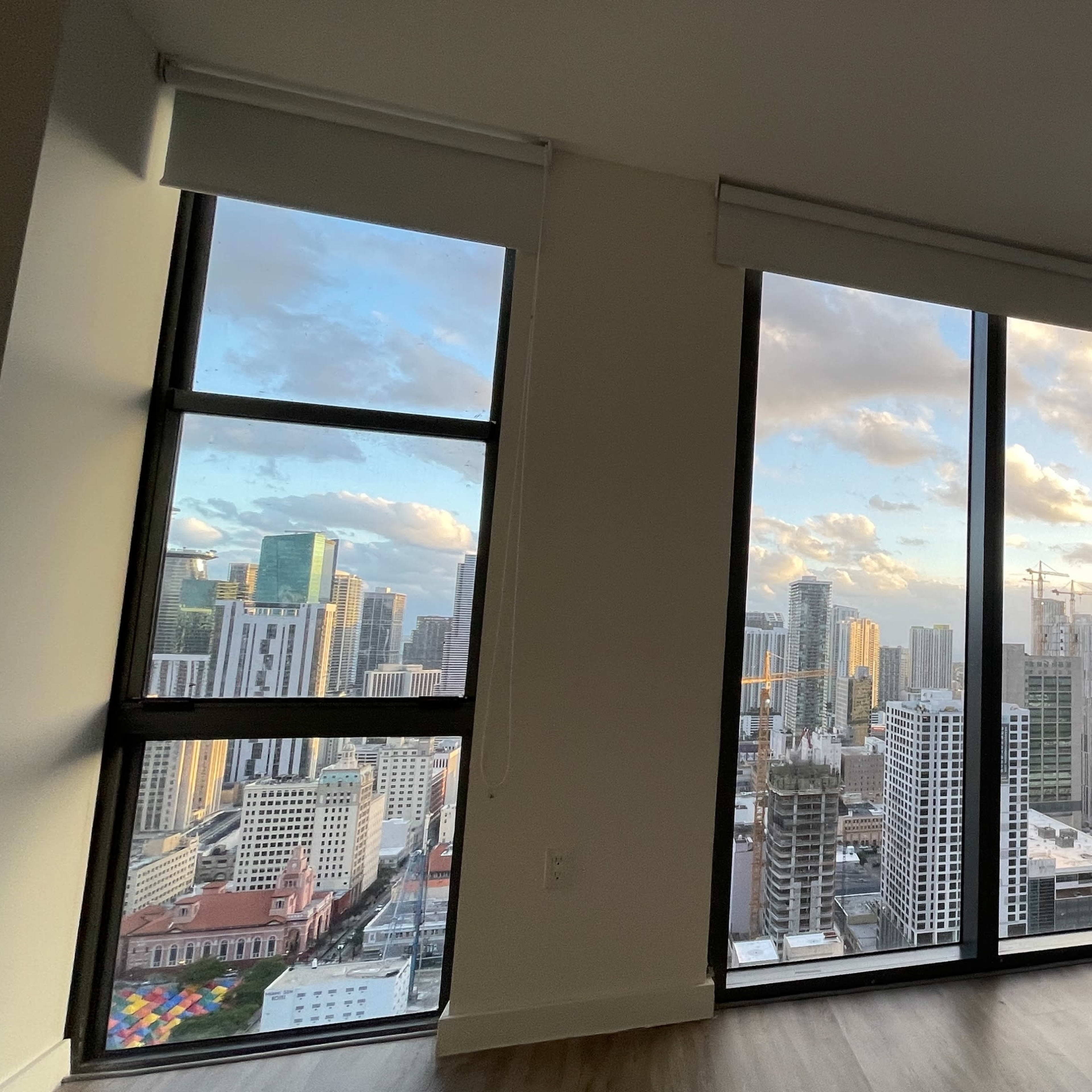A modern apartment with large windows overlooking a city skyline at sunset.