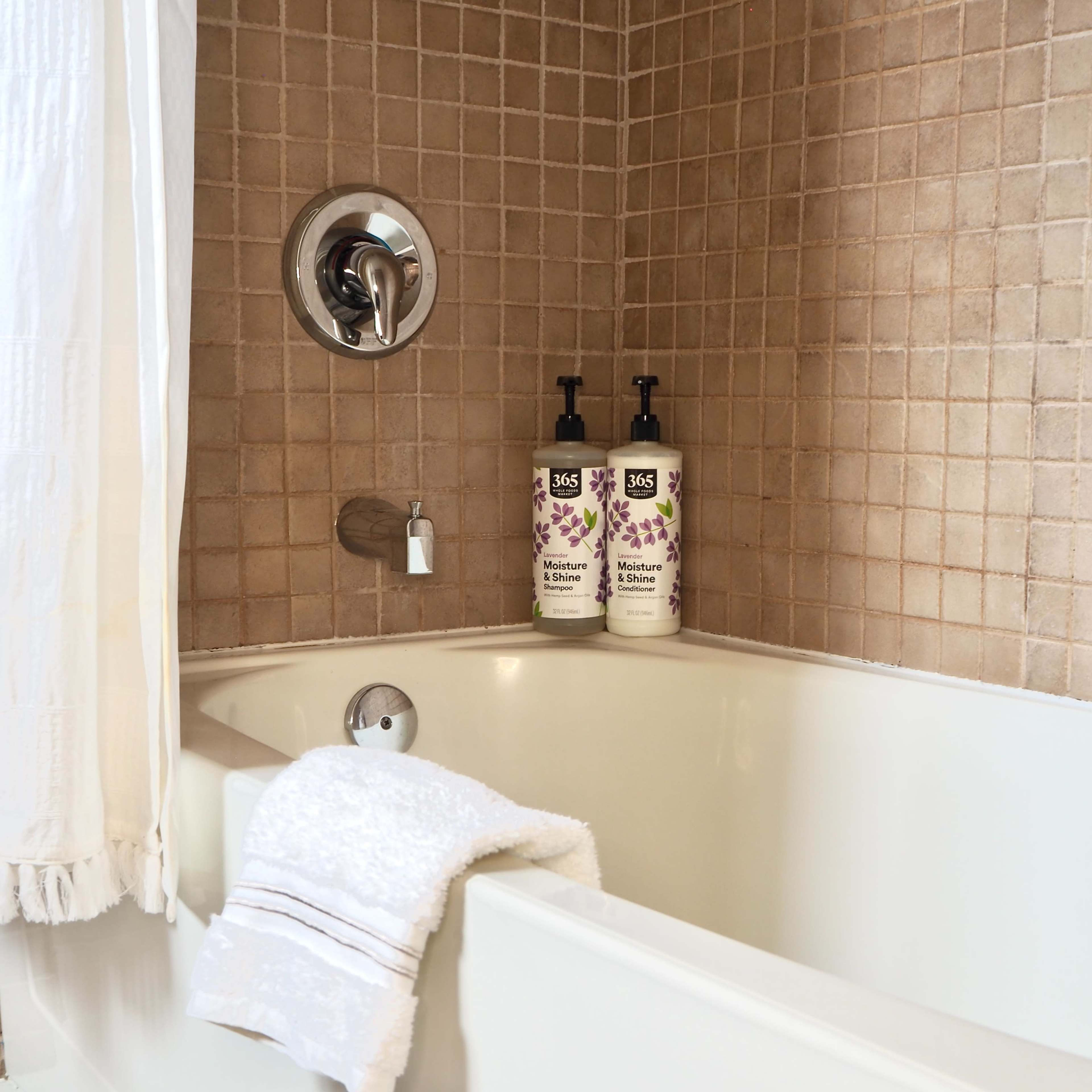 A clean bathtub with two bottles of liquid soap on the edge and a white towel hanging nearby.
