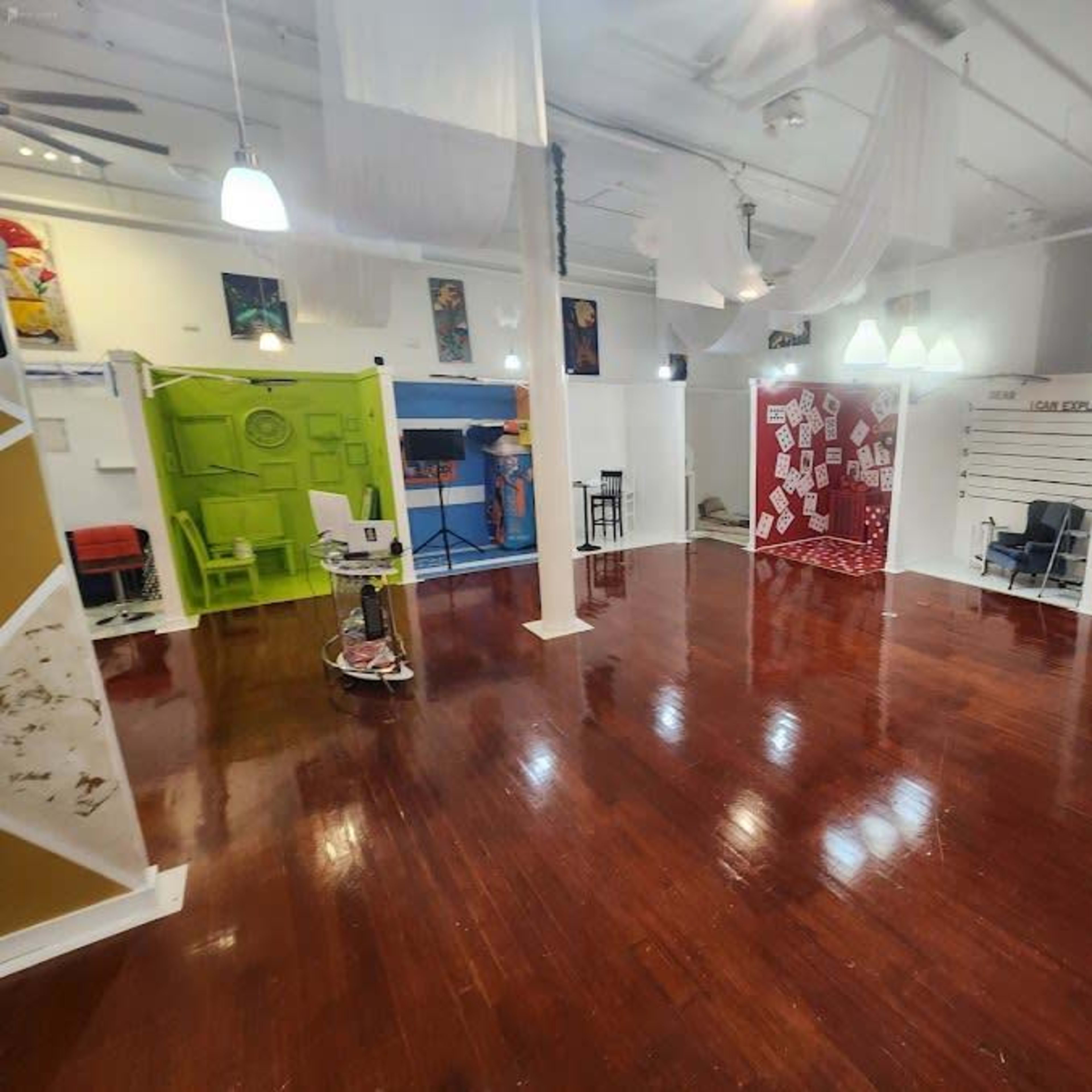 An empty, well-lit interior space with polished wooden floors, featuring colorful walls and different sections enclosed by partitions.