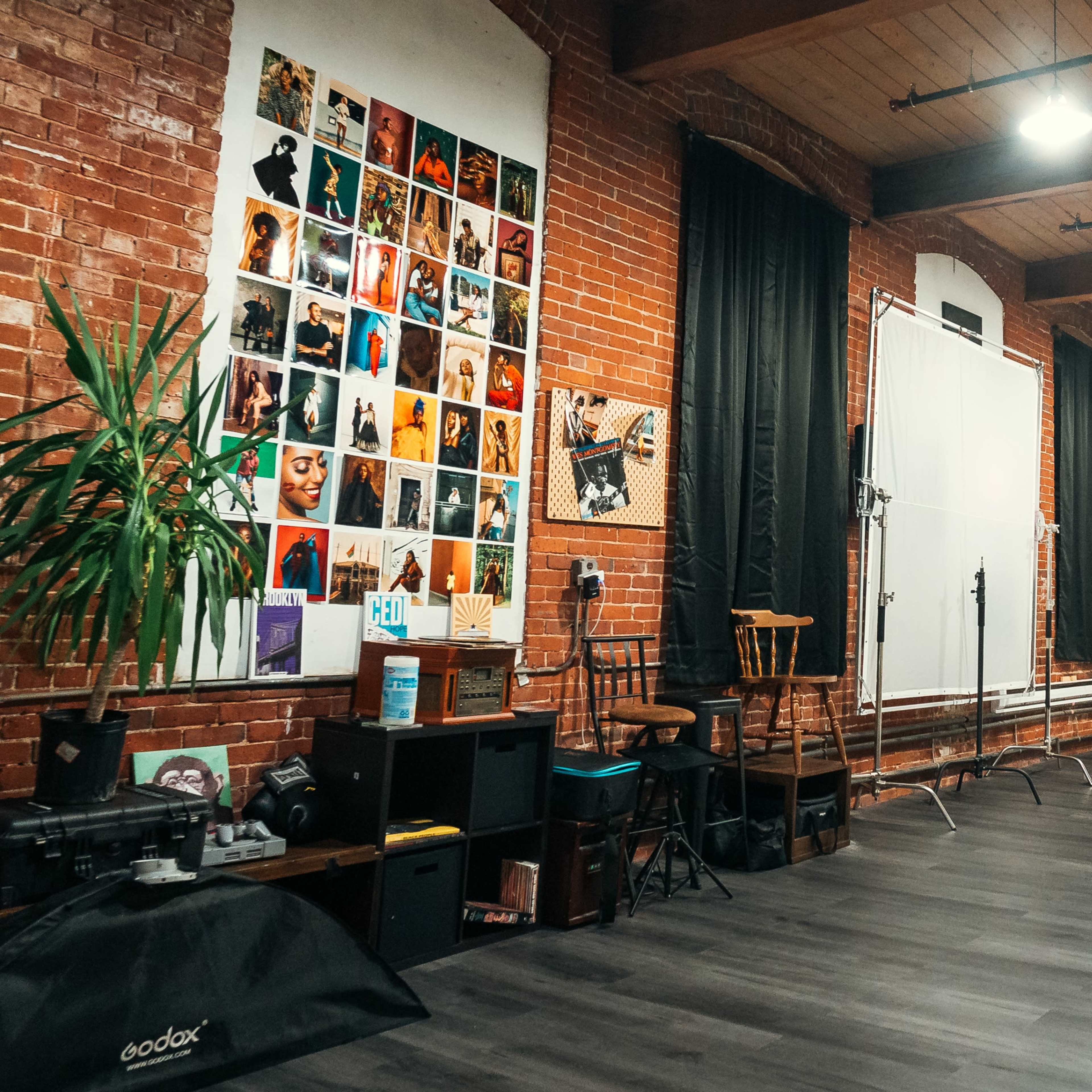 A photography studio with brick walls, a collection of framed photos, a white backdrop, and various lighting equipment.