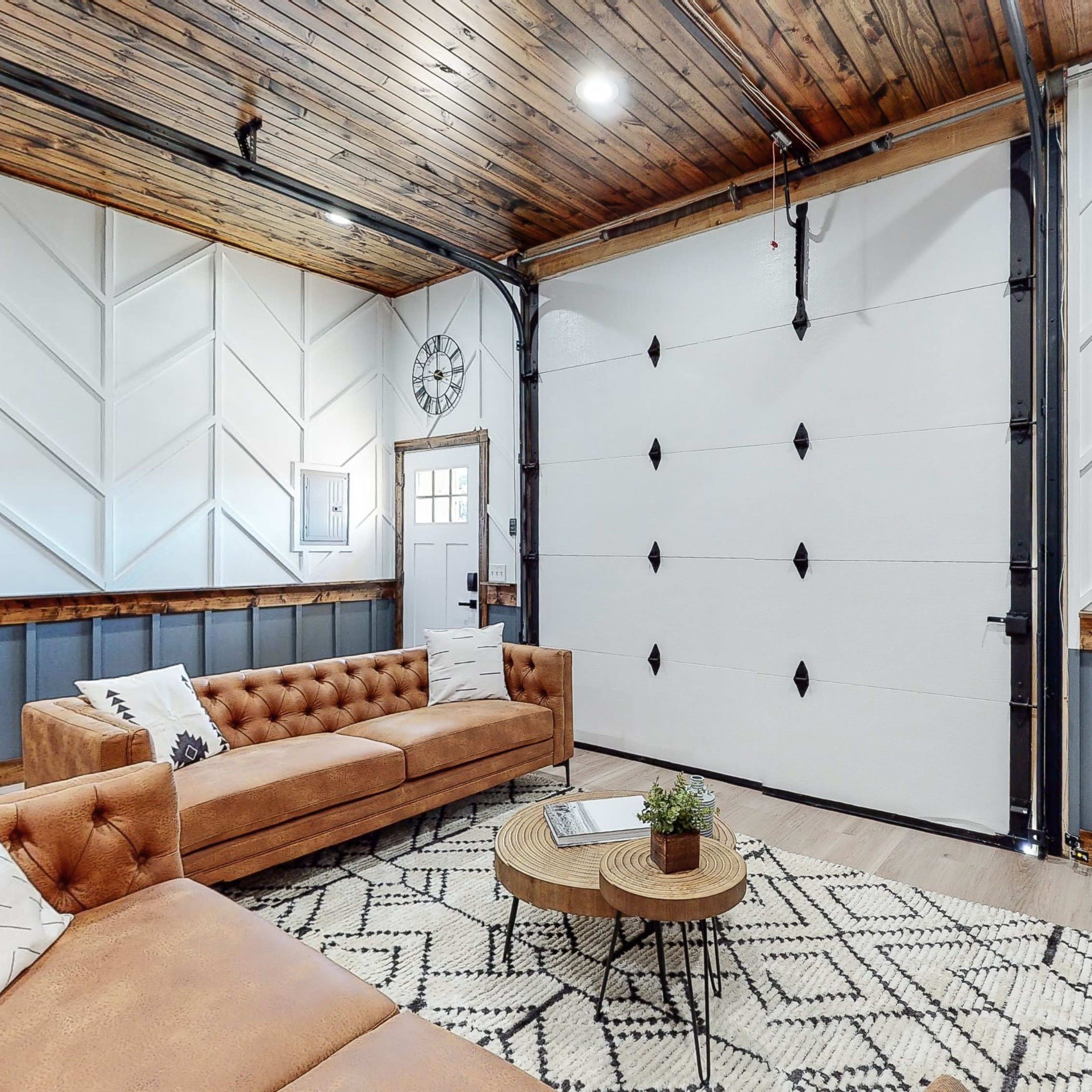 The room features a cozy seating area with a brown tufted sofa, a round coffee table, and a wall-mounted coat rack, all set against a backdrop of wooden ceiling and patterned walls.