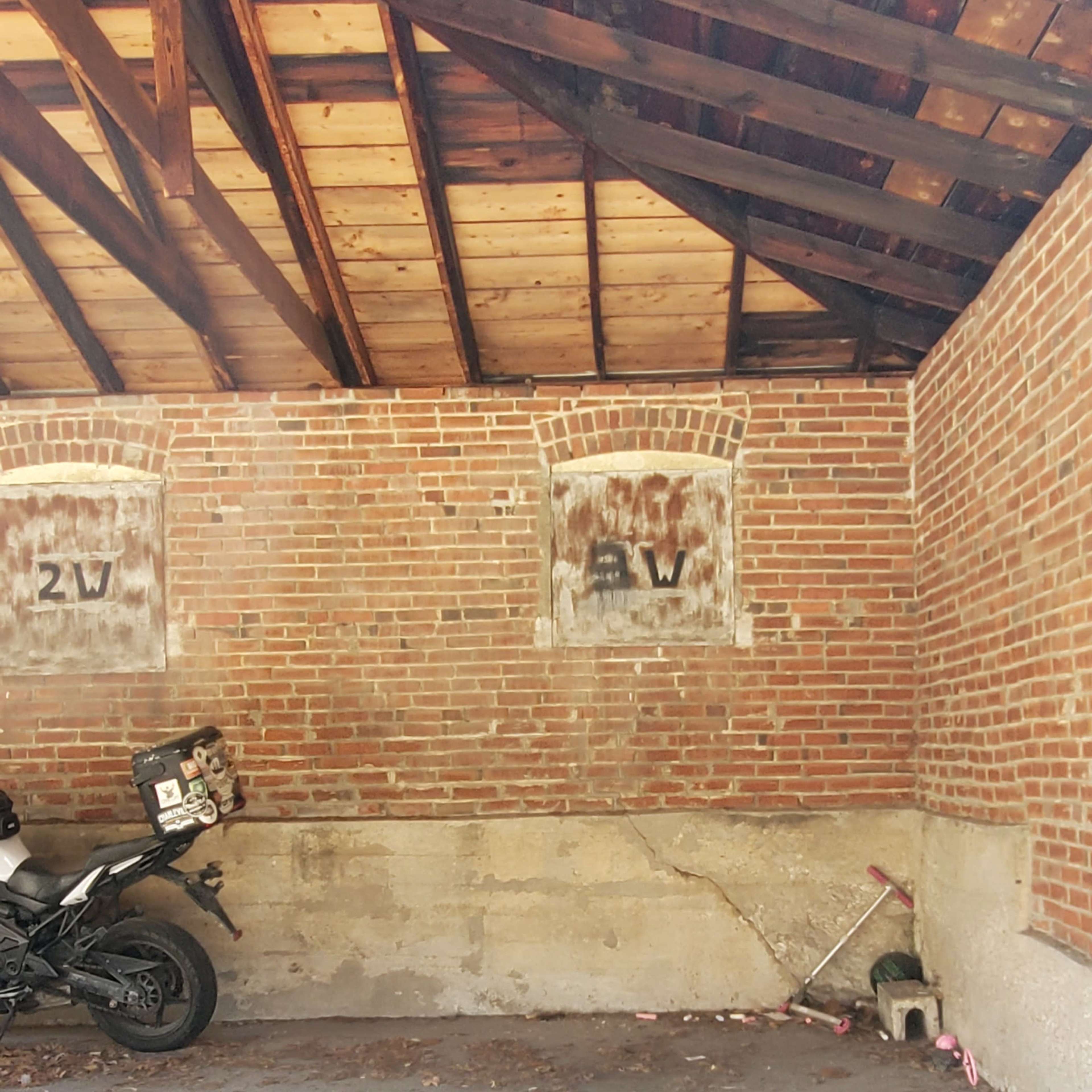 An empty garage with a motorcycle parked against a brick wall and a small tool nearby.