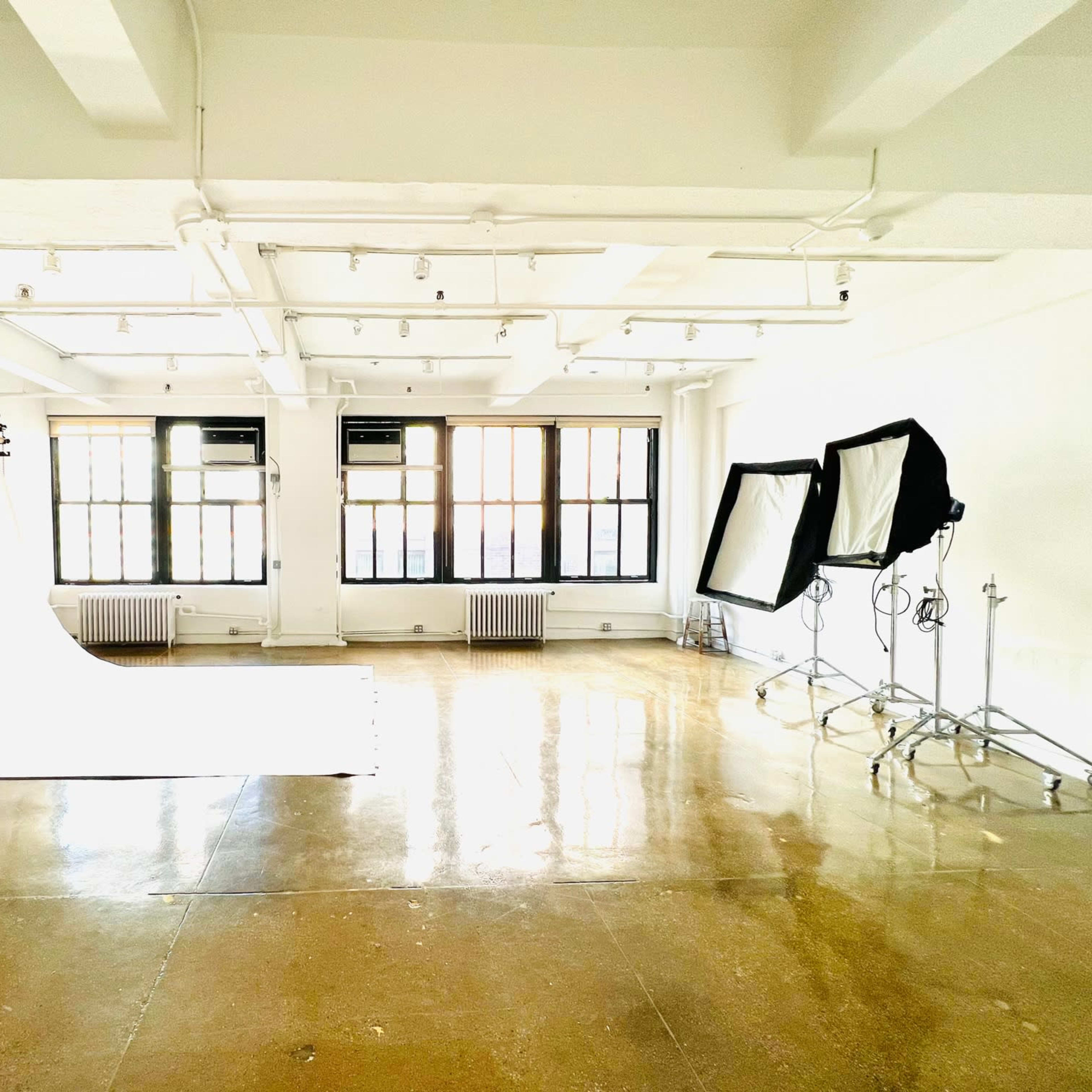A well-lit photography studio featuring a white backdrop, large softbox lights, and multiple windows.