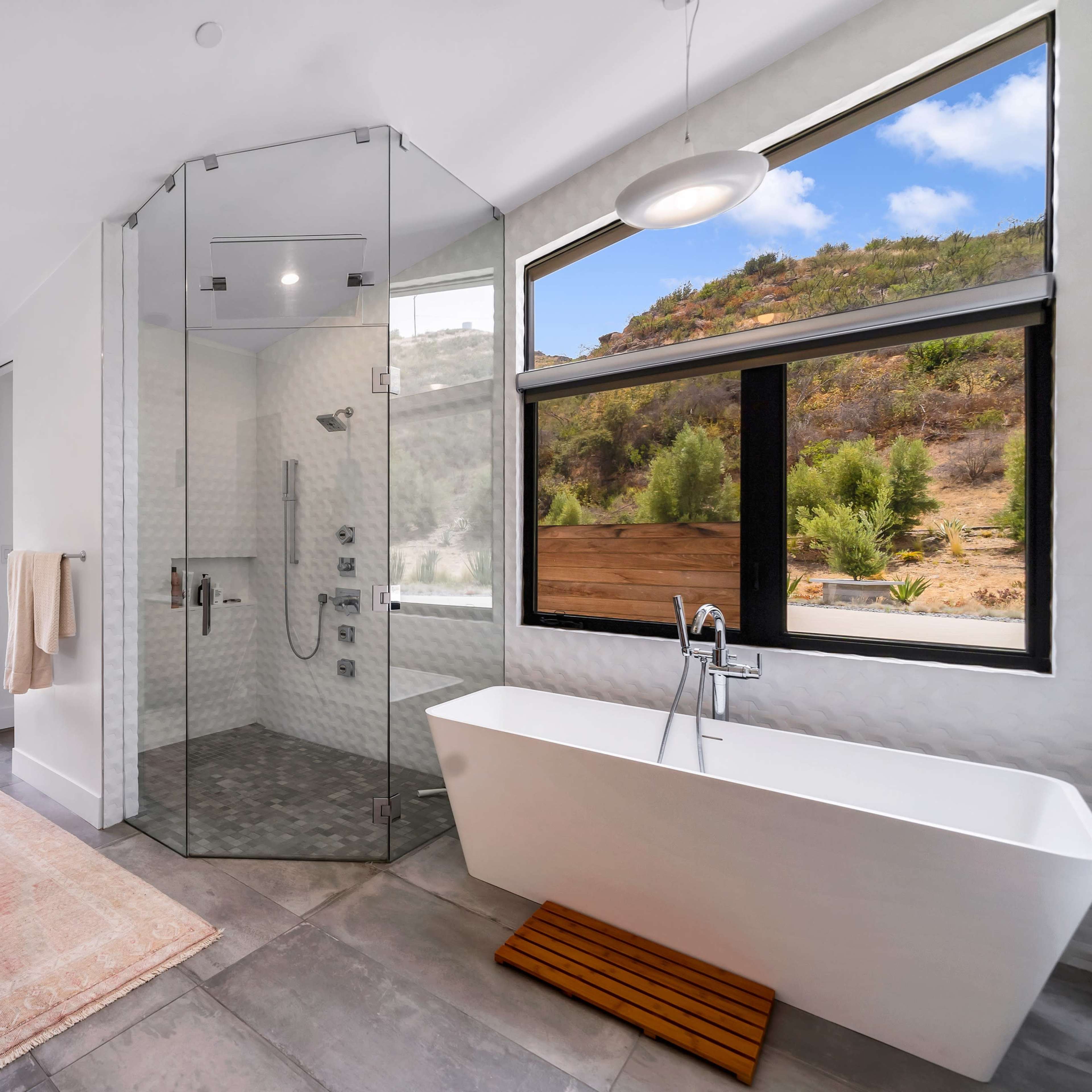 A modern bathroom featuring a glass-enclosed shower, a freestanding bathtub, and large windows overlooking a landscape.