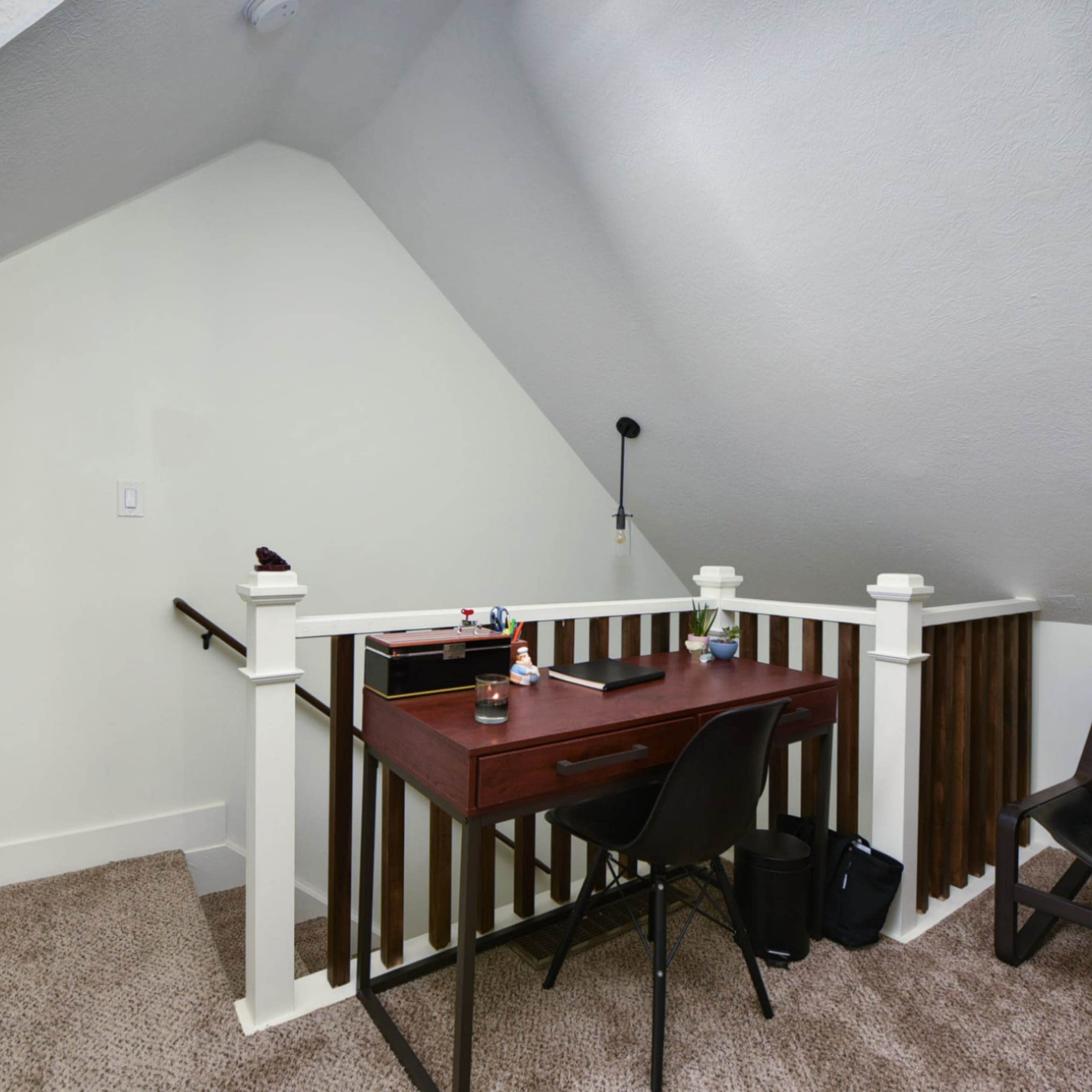 A small workspace with a desk and chair positioned near a staircase in a room with sloped ceilings.
