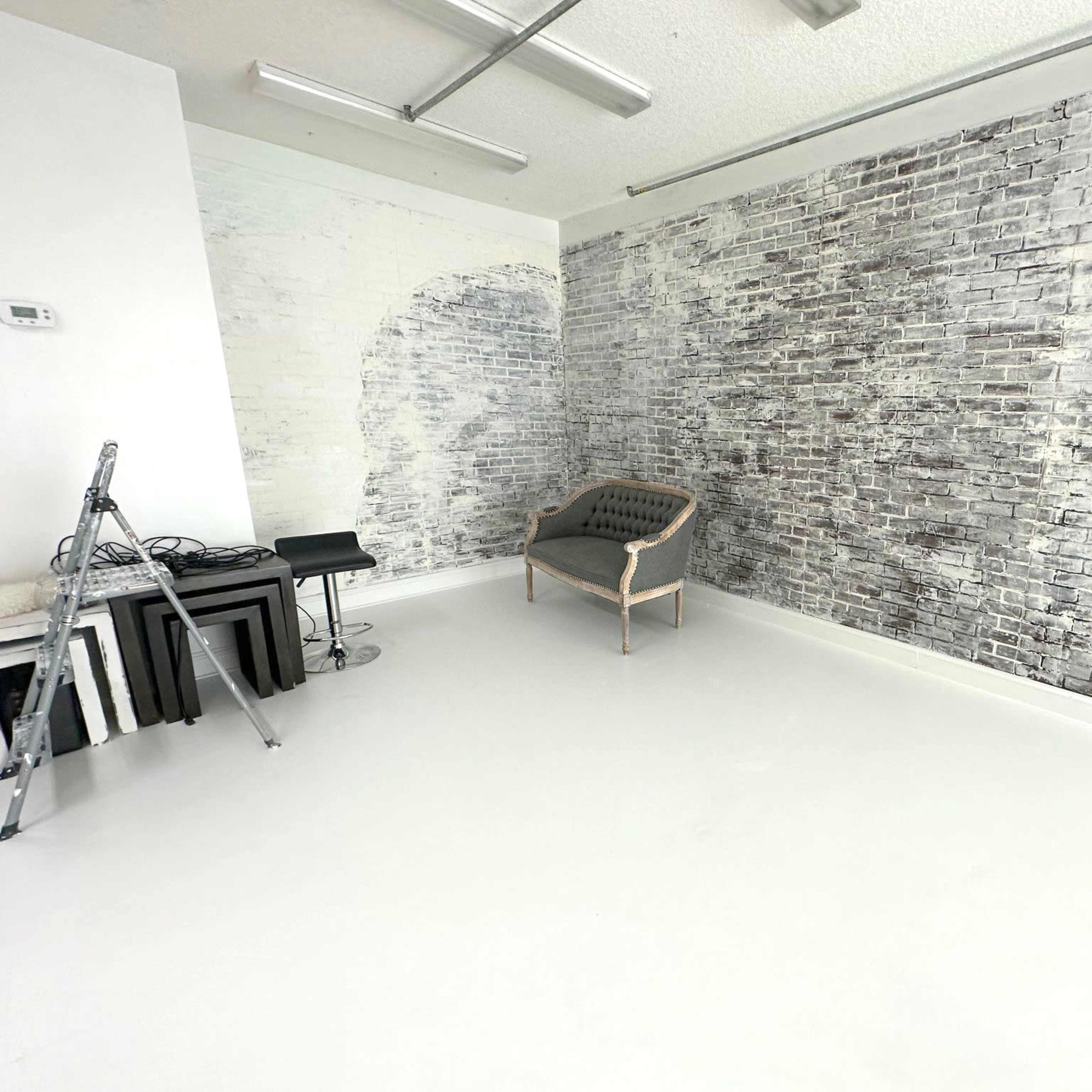 A room with a white floor, a sofa against a textured brick wall, and a few pieces of furniture including a ladder and side tables.