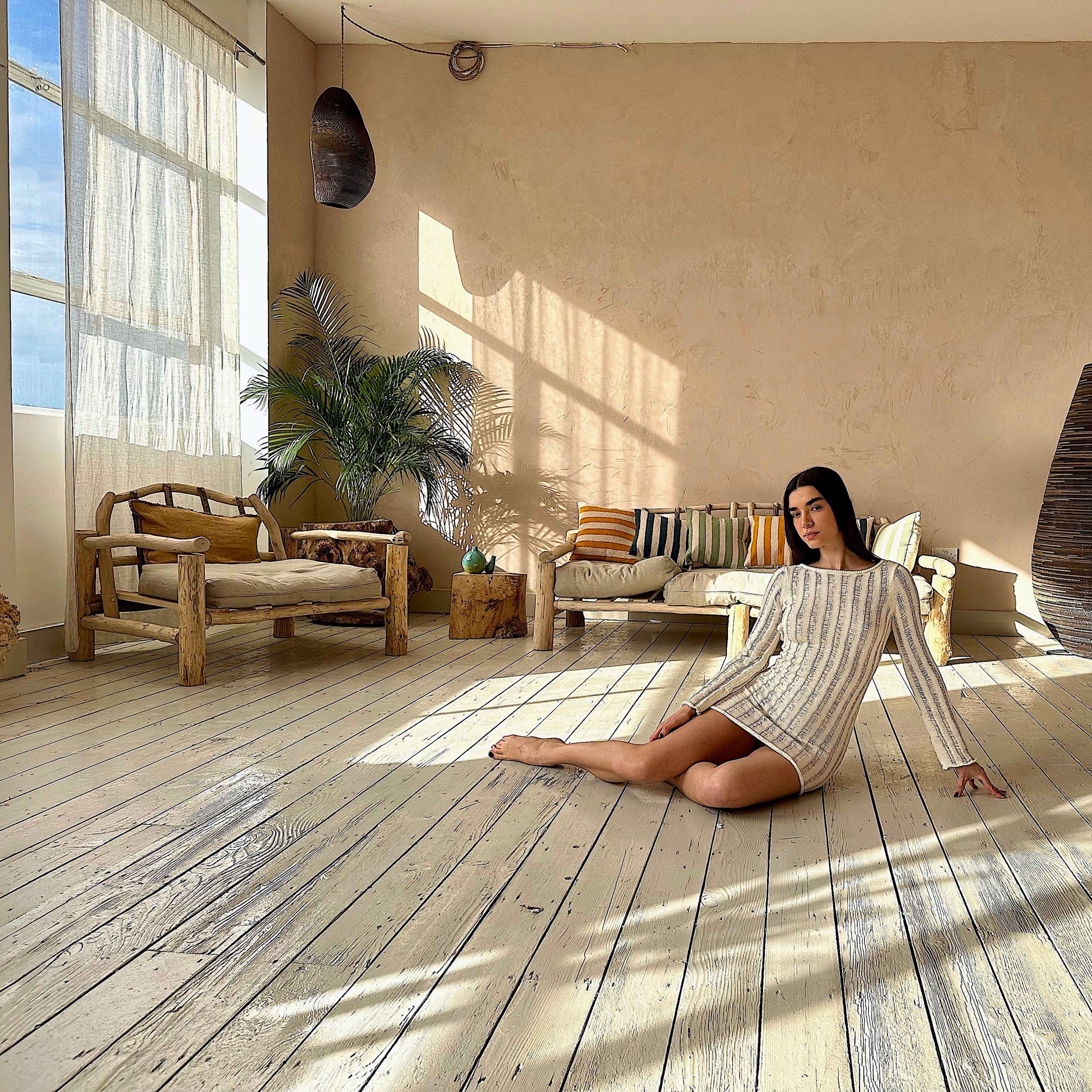 A person sits on the floor of a spacious, lightly decorated room with natural light streaming through large windows.