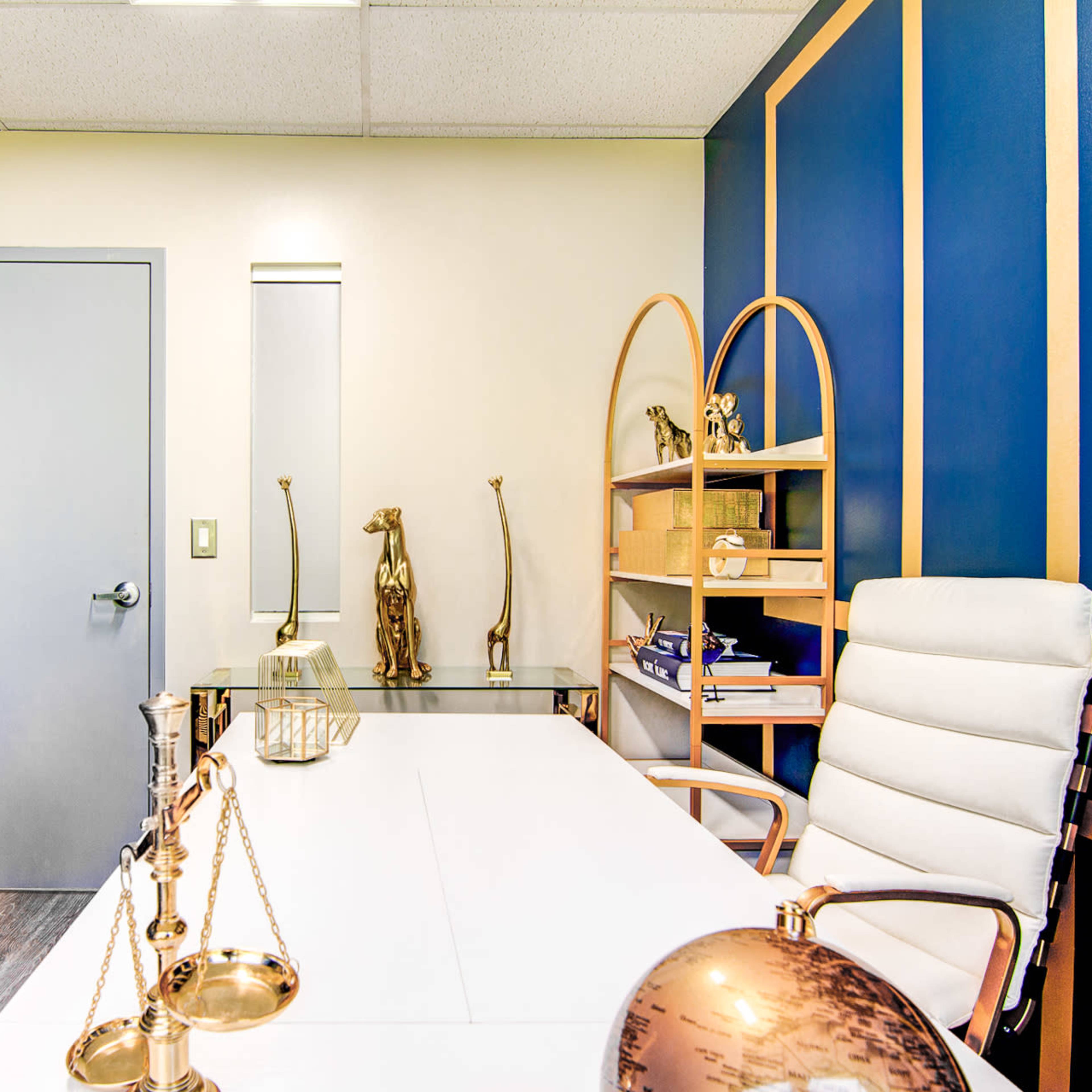 A modern office space featuring a white desk, a leather chair, blue walls, and various decorative items, including sculptures and a globe.