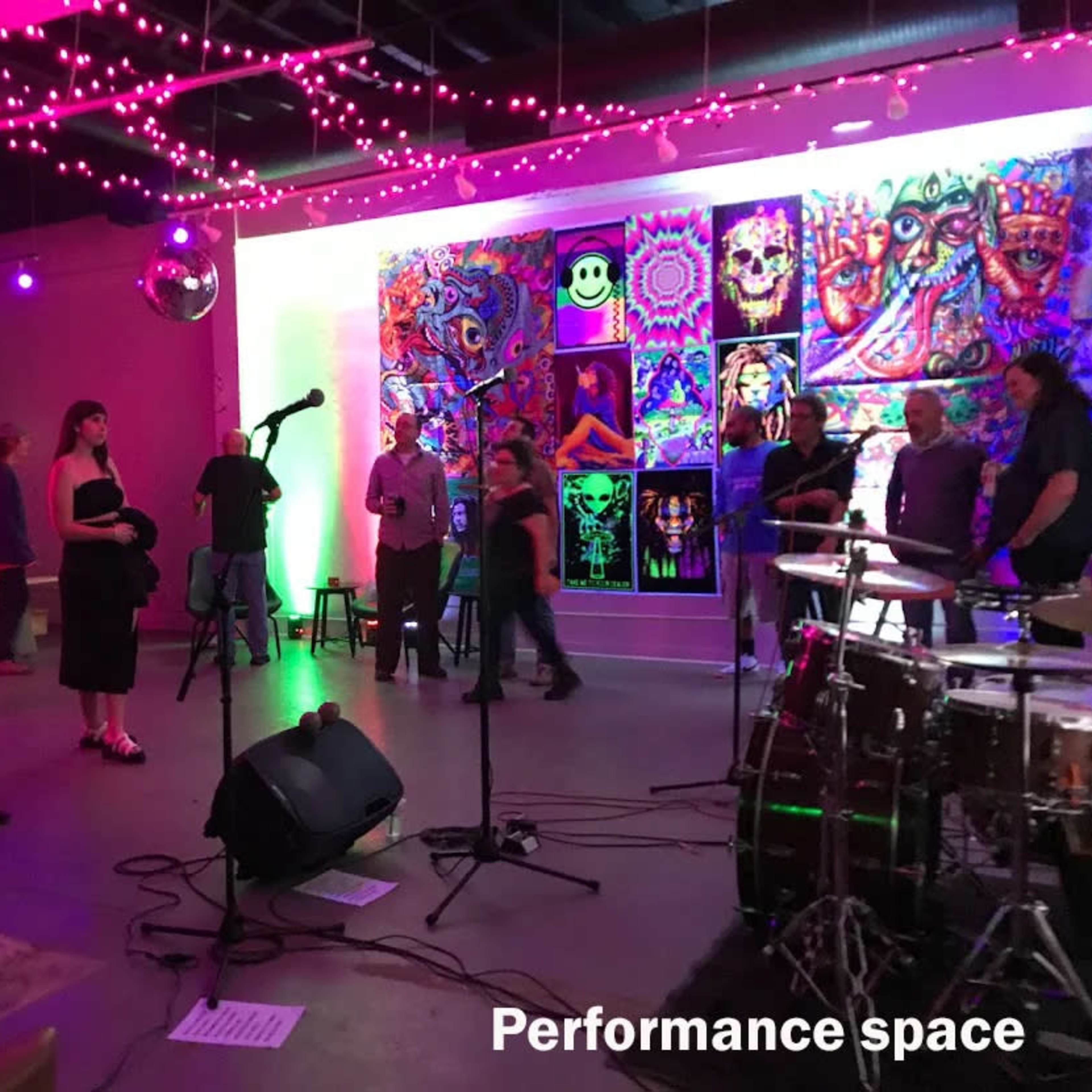 A vibrant performance space filled with people, illuminated by colorful lights and featuring a decorated wall with artwork.
