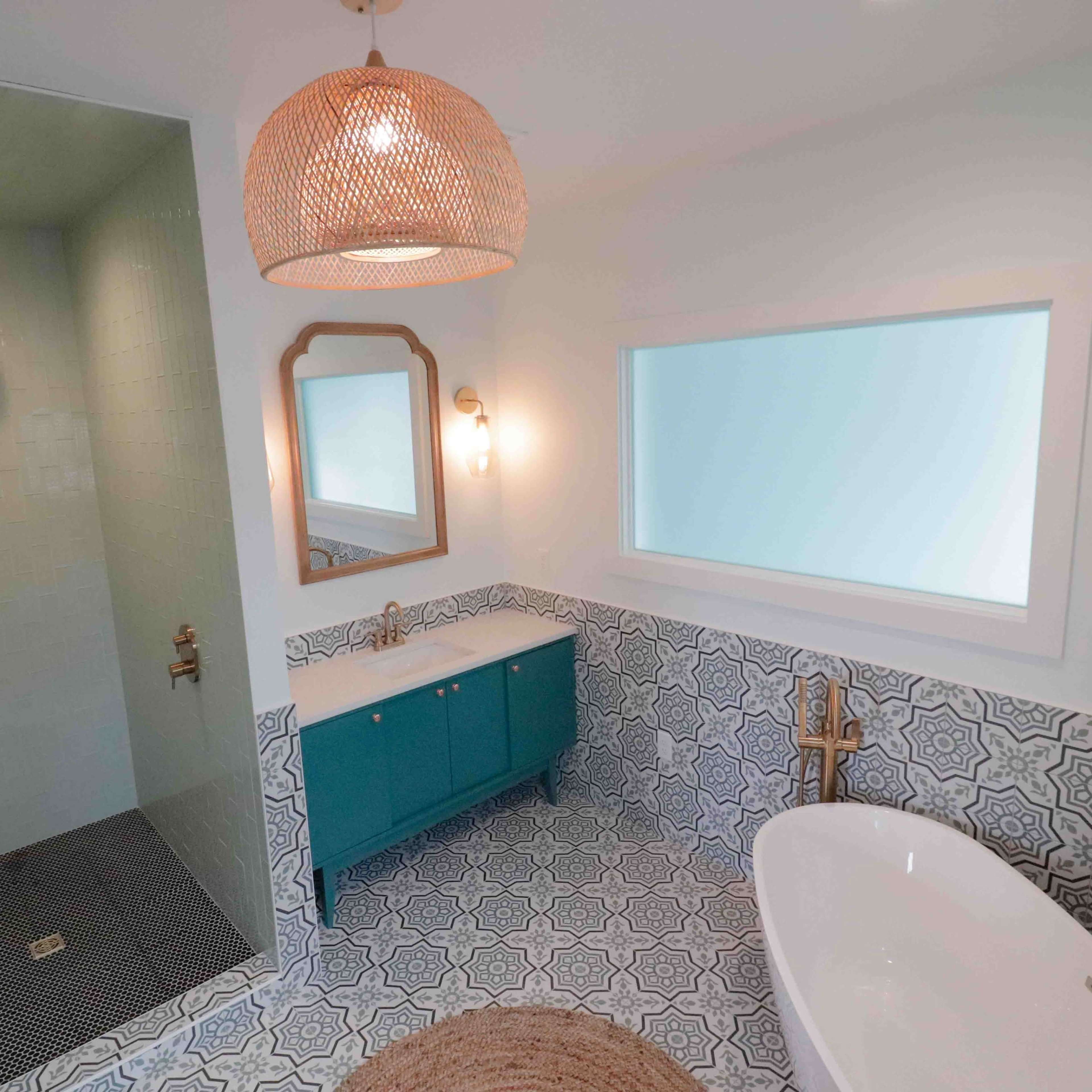 A modern bathroom featuring a glass shower, a freestanding bathtub, a blue vanity with a sink, and patterned tiles on the floor and walls.