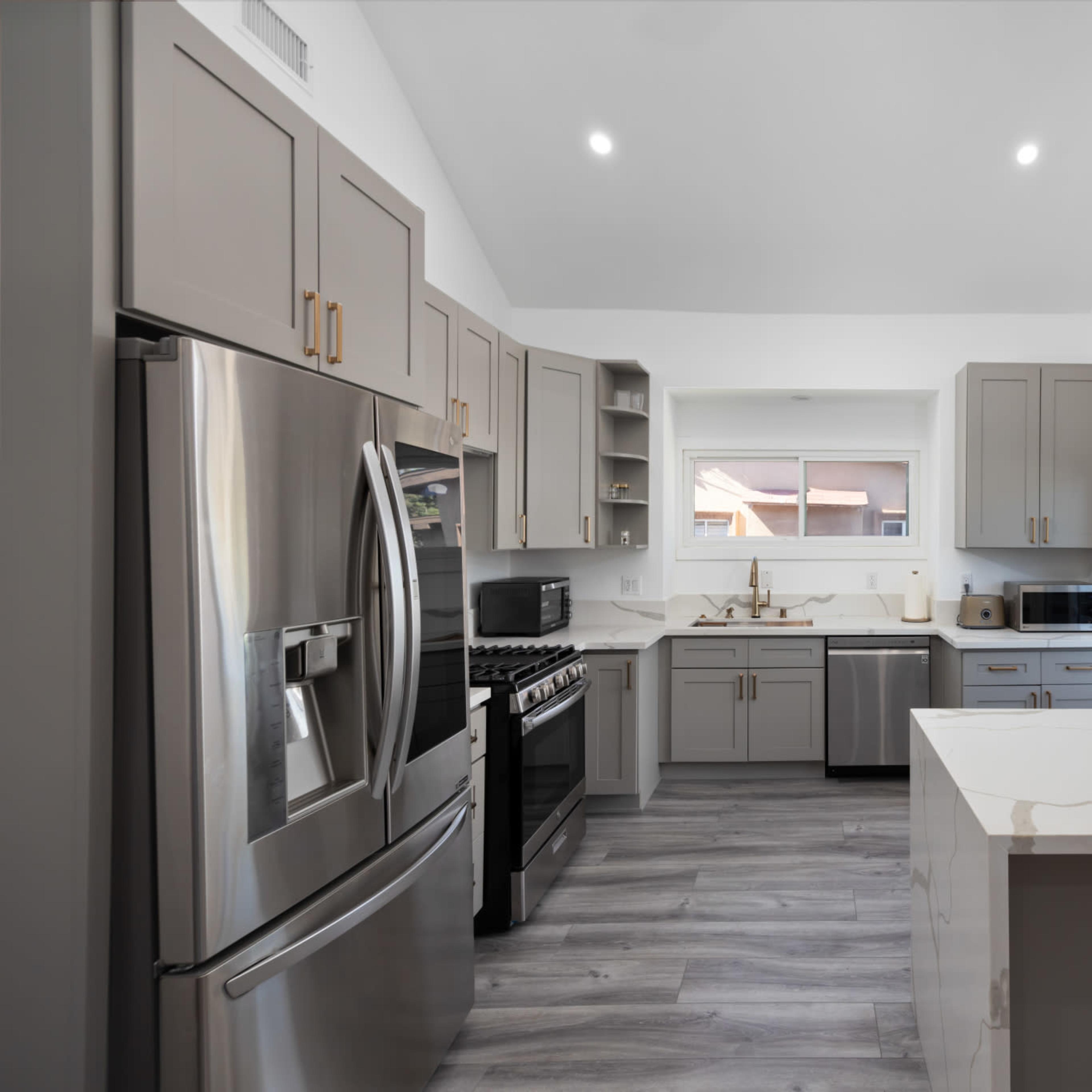 A modern kitchen featuring gray cabinetry, stainless steel appliances, and a large island with a white countertop.