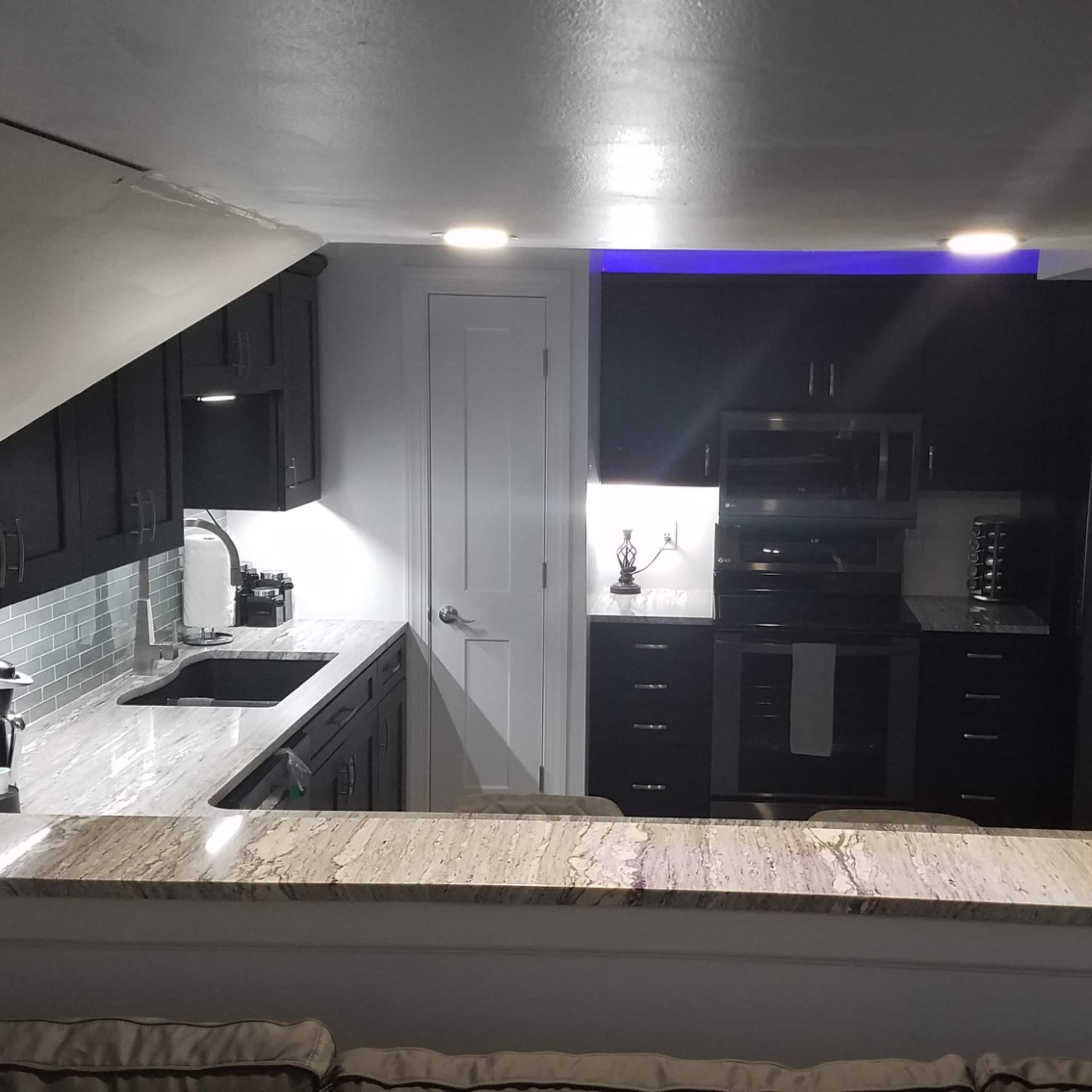 A modern kitchen with dark cabinets, a granite countertop, and stainless steel appliances, illuminated by recessed lighting.