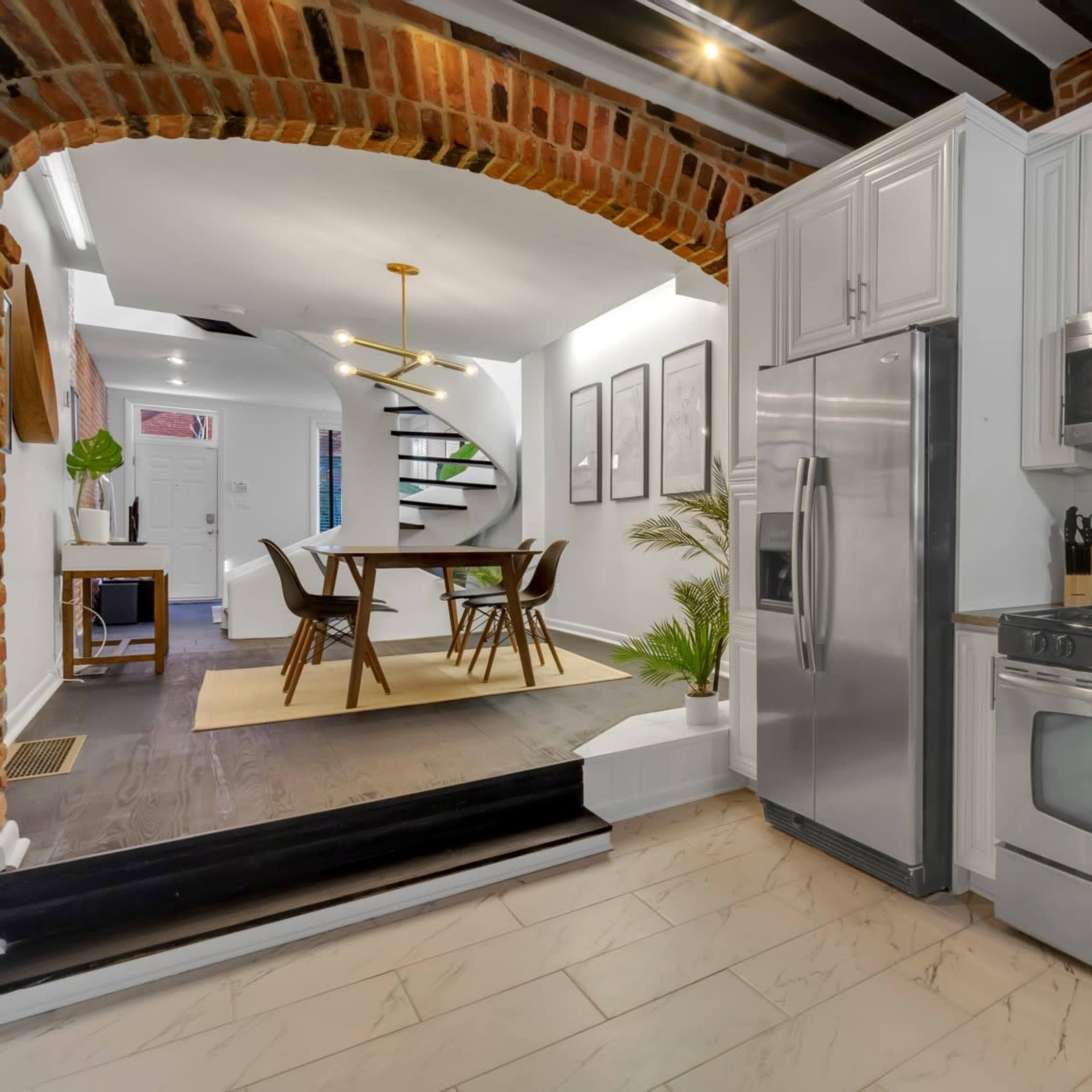 A modern kitchen features stainless steel appliances, white cabinets, and a tile floor, with an archway leading to a dining area.