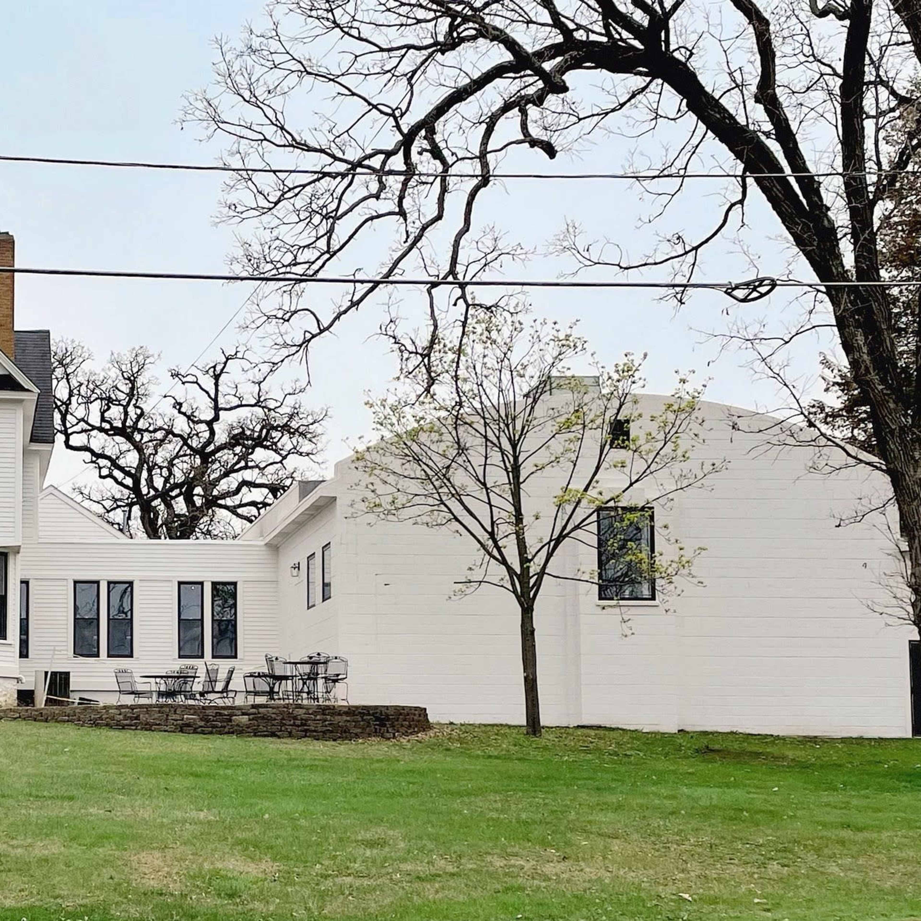 A large two-story house with a flagpole stands next to a smaller one-story building on a grassy lawn.