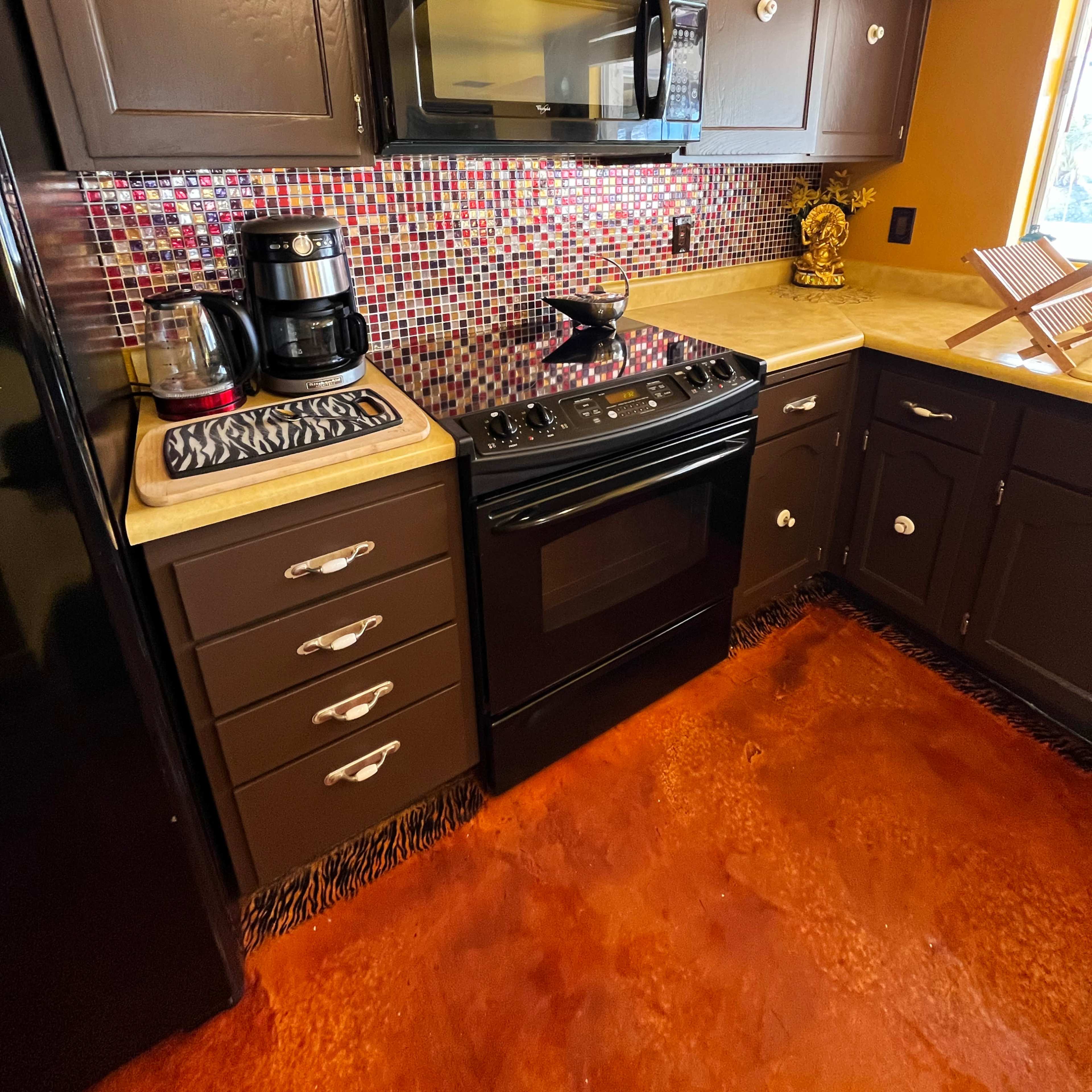 A modern kitchen features dark cabinetry, a black microwave and stove, and a mosaic backsplash with colorful tiles.