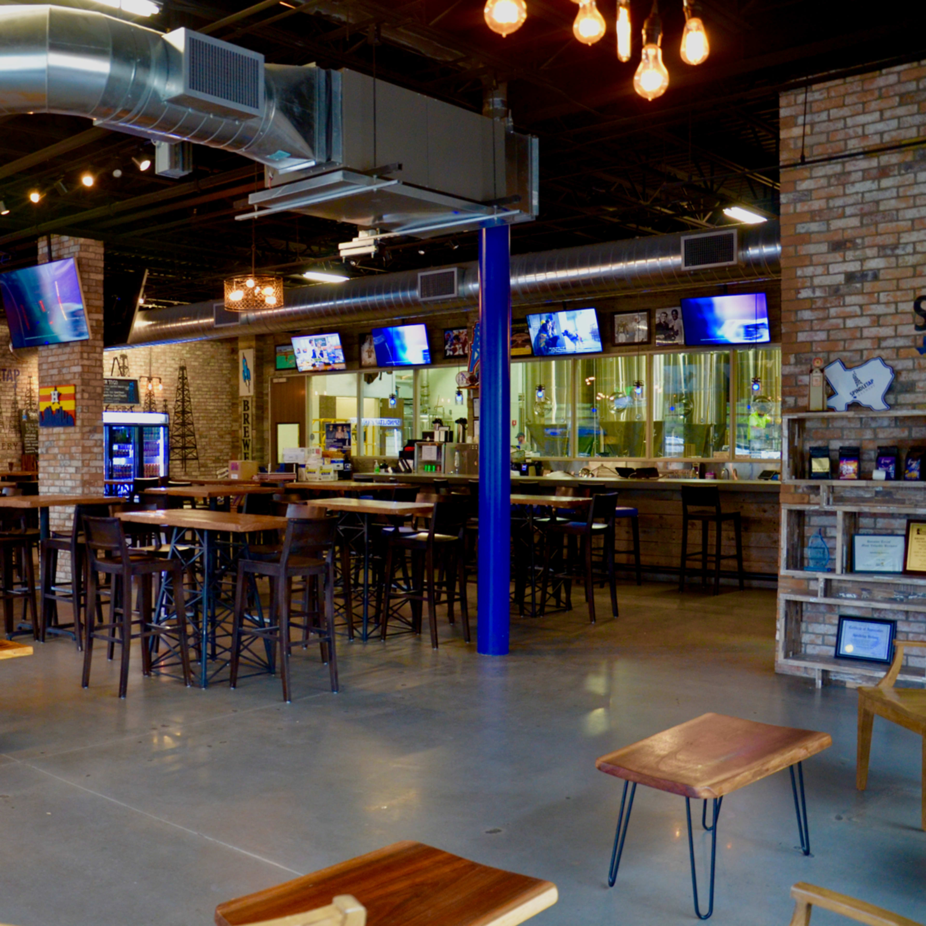 A spacious, industrial-style restaurant with wooden tables and a bar area, featuring exposed brick walls and metal ductwork.