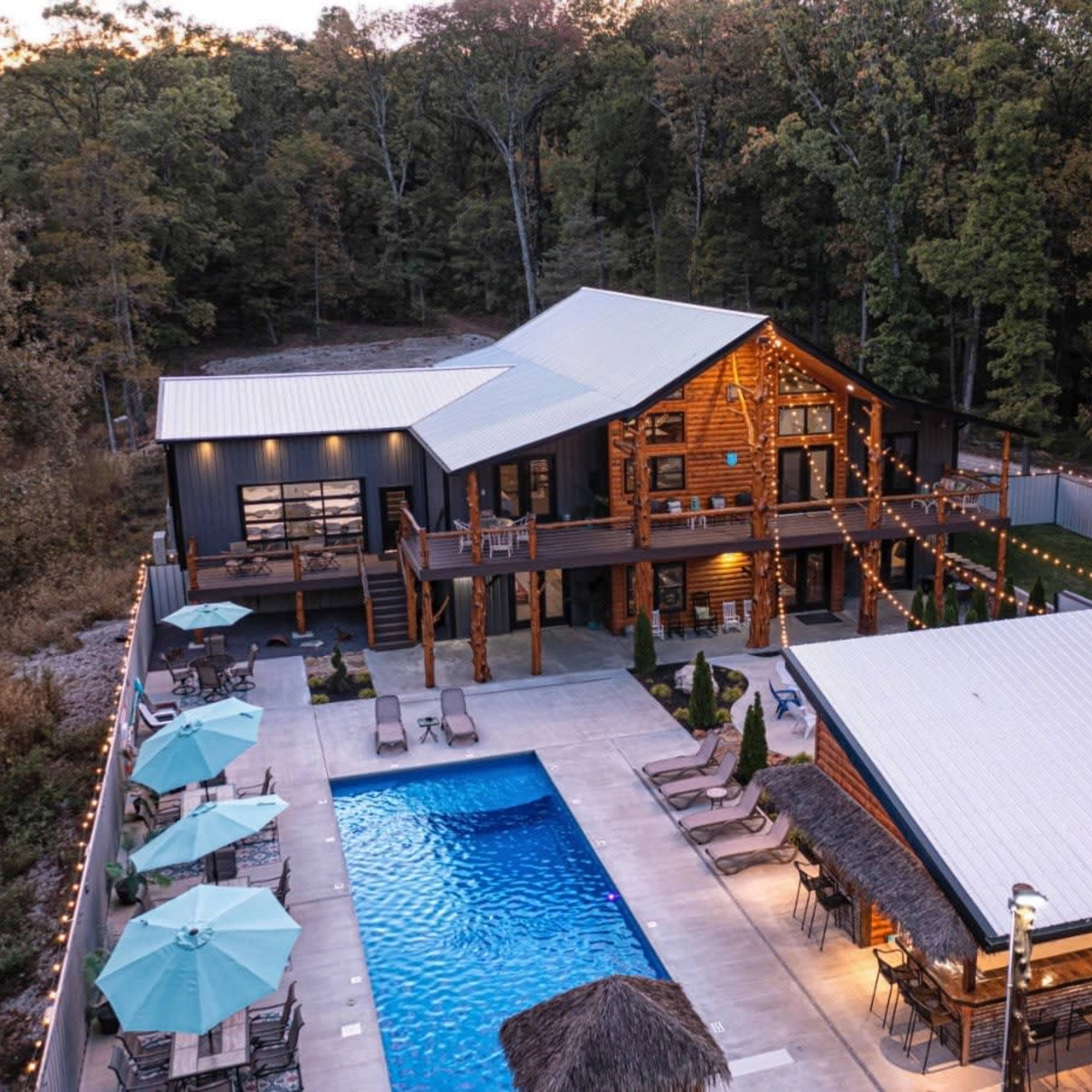 A modern lodge-style home with a large pool and surrounding outdoor seating area, set in a wooded environment.