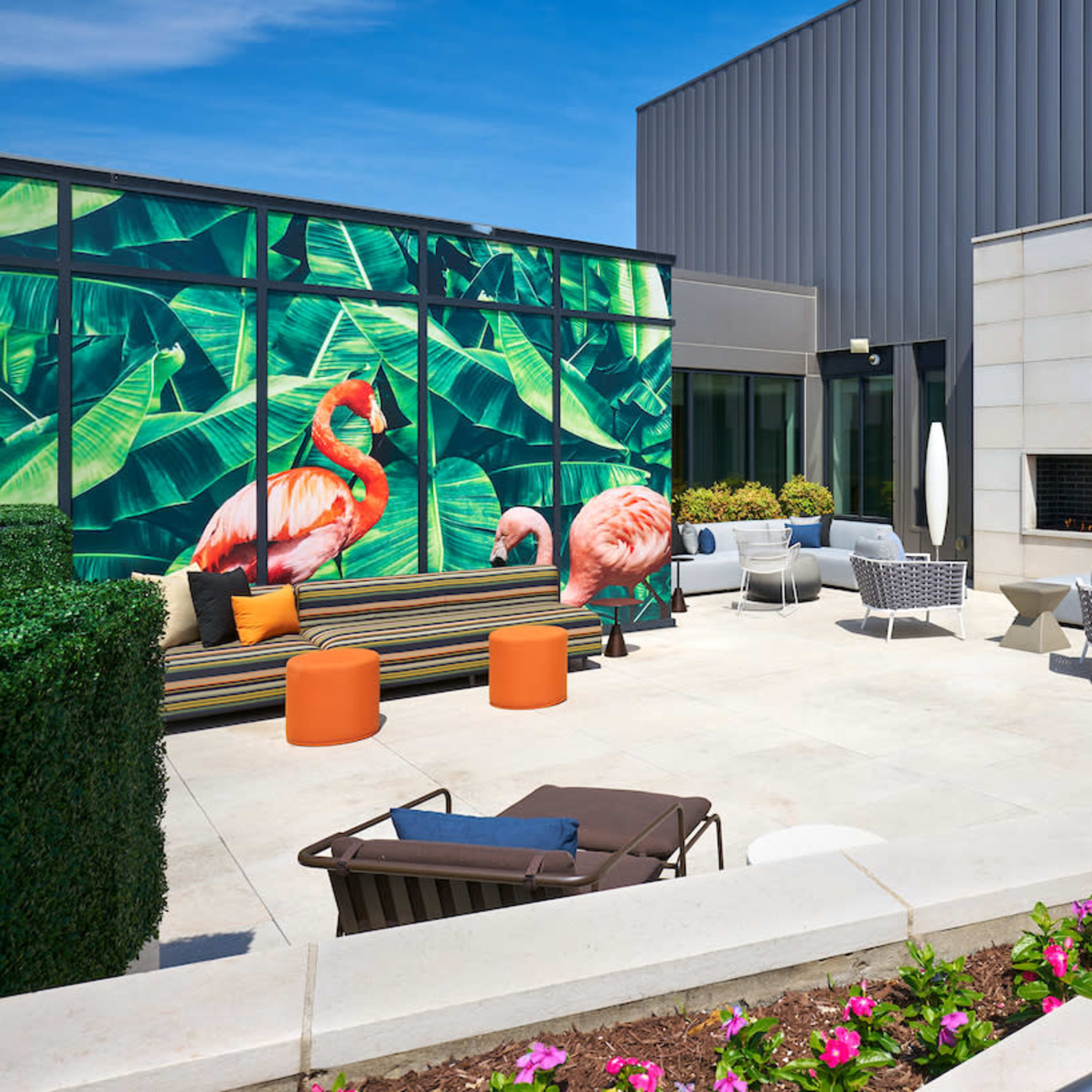 A rooftop patio featuring colorful seating, a decorative mural of flamingos, and a modern fireplace.