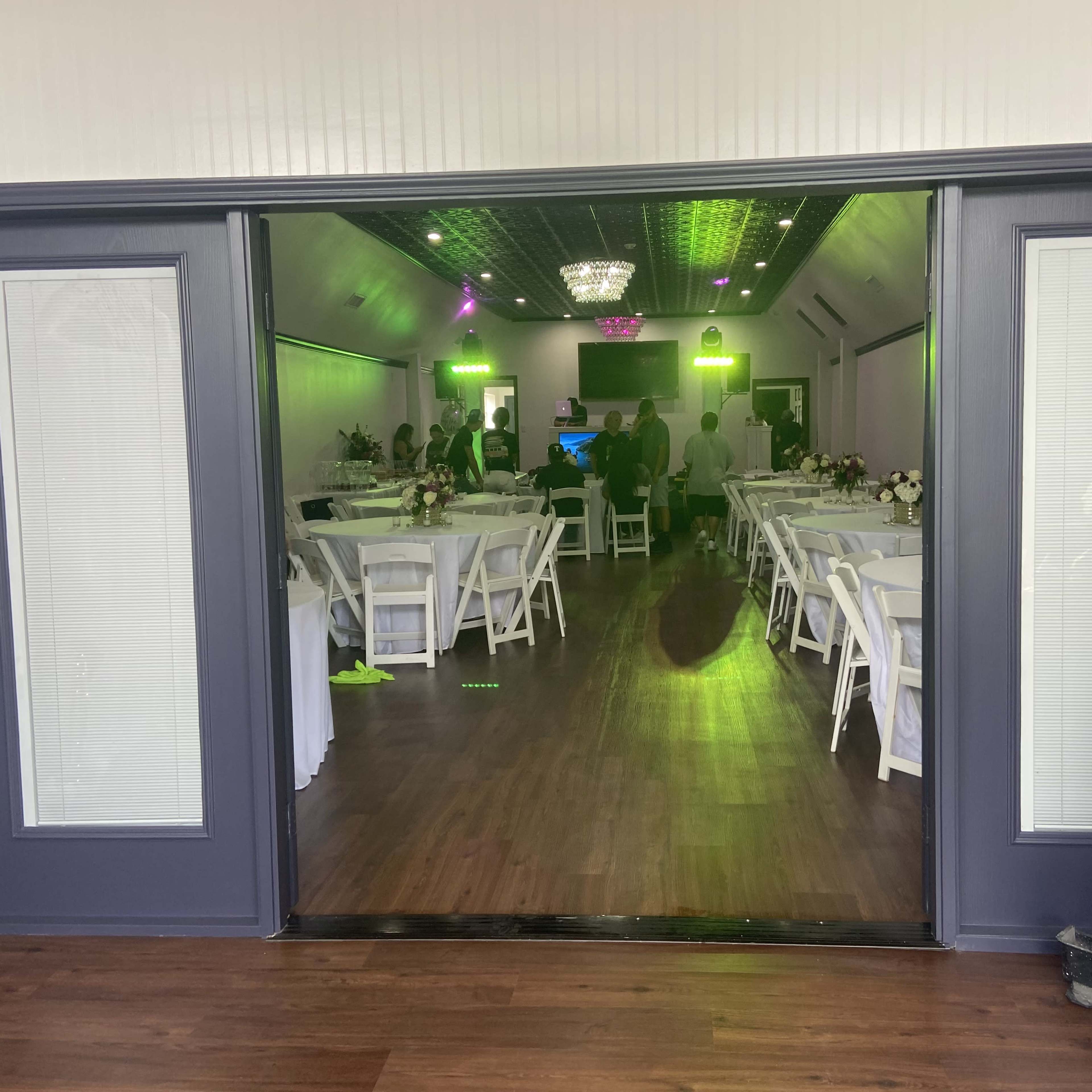 The entrance to an indoor venue featuring tables and chairs arranged for an event, with green lighting and decorations visible inside.